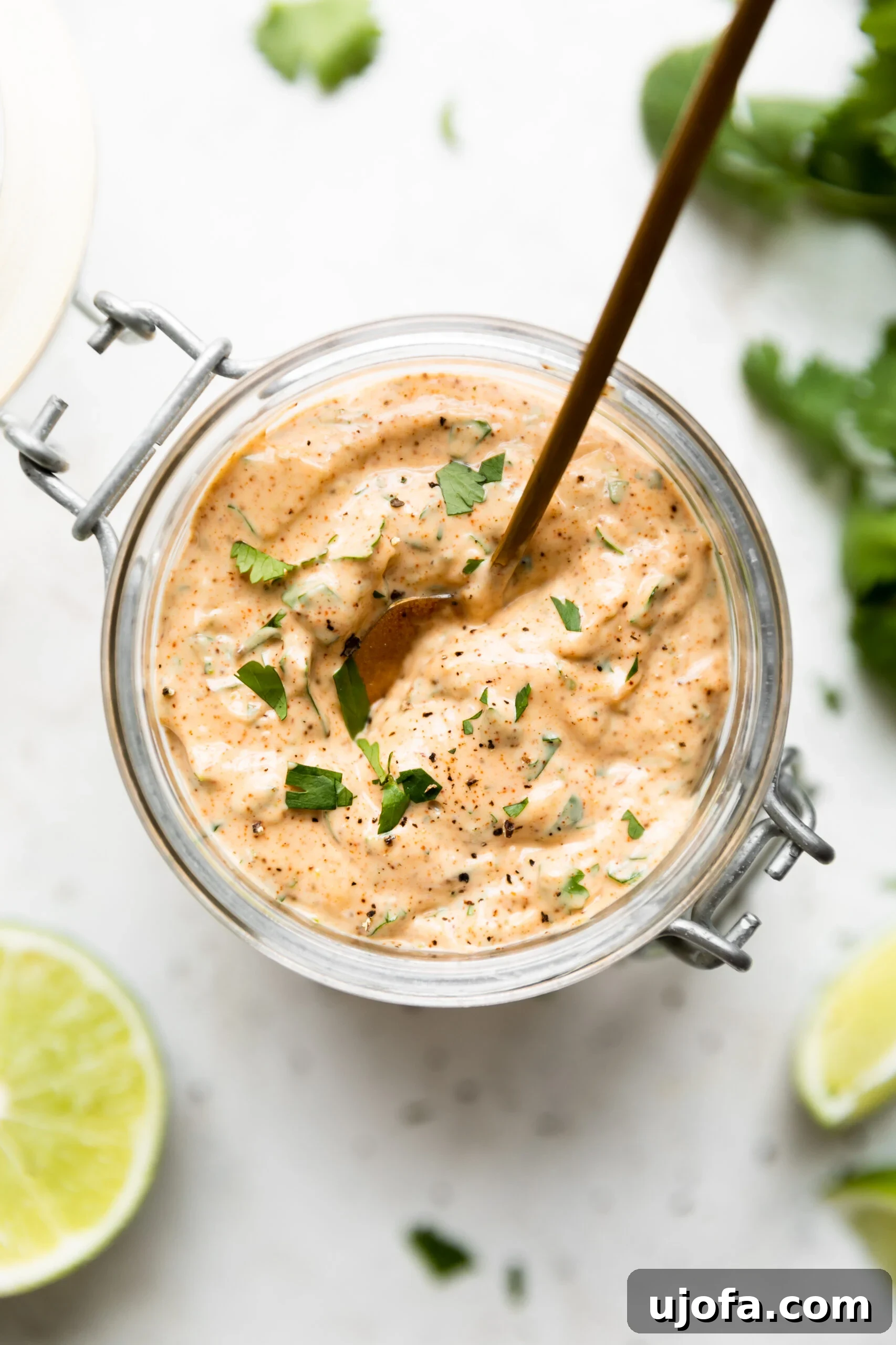 A small glass bowl filled with vibrant green cilantro lime sauce, perfectly complemented by fresh lime wedges nearby.