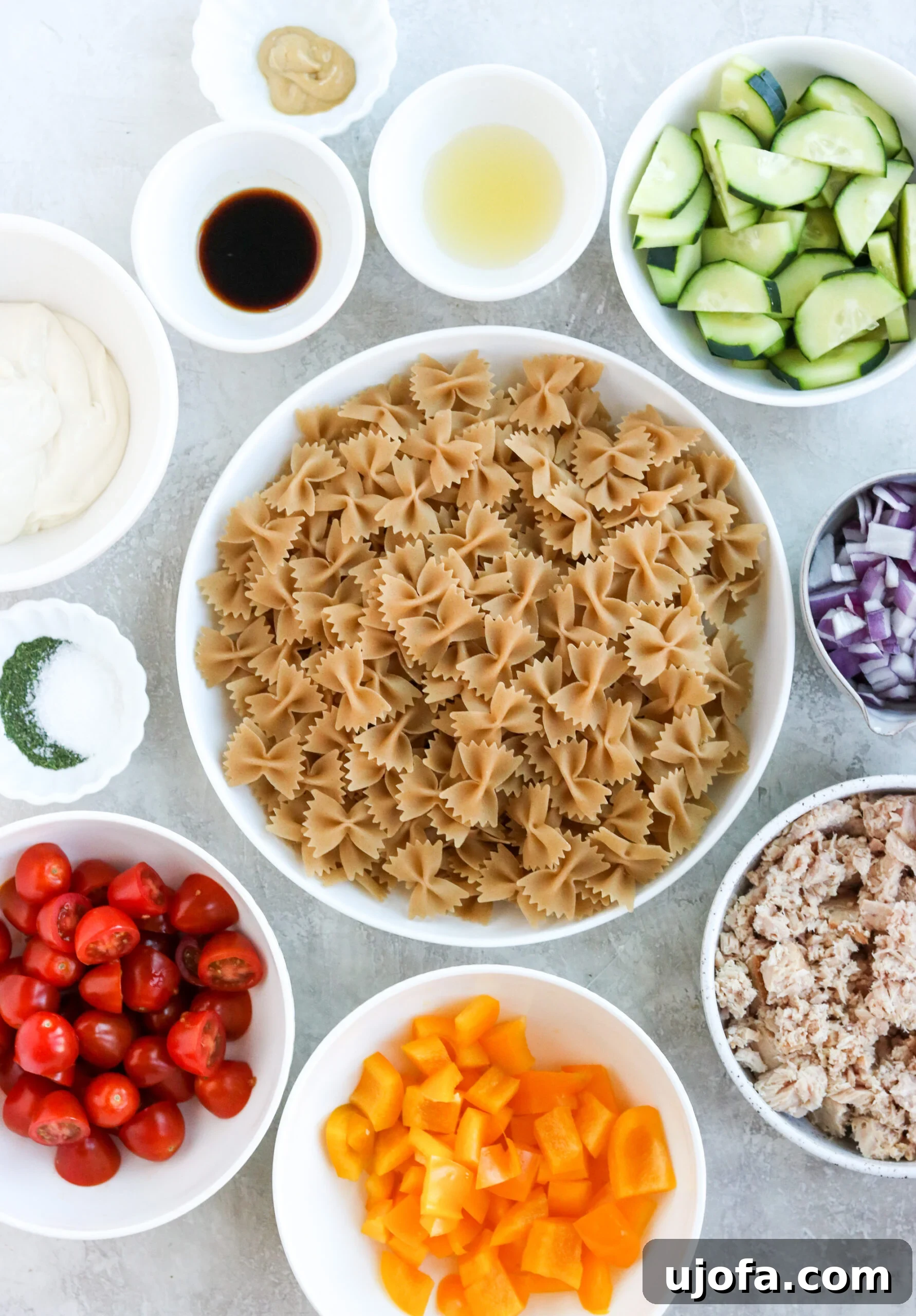 A collection of fresh ingredients laid out, including gluten-free pasta, canned tuna, and various chopped vegetables, ready to be assembled for a healthy pasta salad.