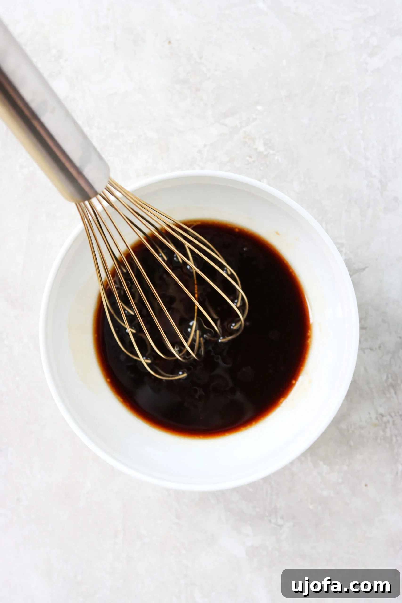 A person's hand whisking a vibrant, homemade stir-fry sauce in a small white bowl, ready to be poured over sizzling vegetables.