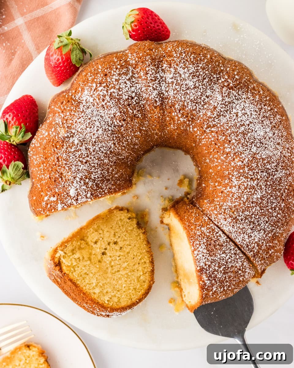 Effortless Gluten-Free Easter Sweets 10 A golden-baked Gluten-Free Kentucky Butter Pound Cake resting on a round white platter, elegantly topped with powdered sugar and garnished with fresh, vibrant strawberries. A slice has been meticulously cut and partially removed, beautifully showcasing the cake's moist, golden interior and tender crumb.
