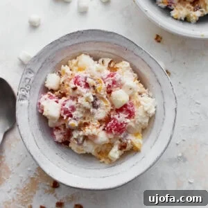 A bowl of ambrosia salad filled with creamy whipped topping, pineapple chunks, mandarin oranges, maraschino cherries, mini marshmallows, shredded coconut, and chopped nuts.