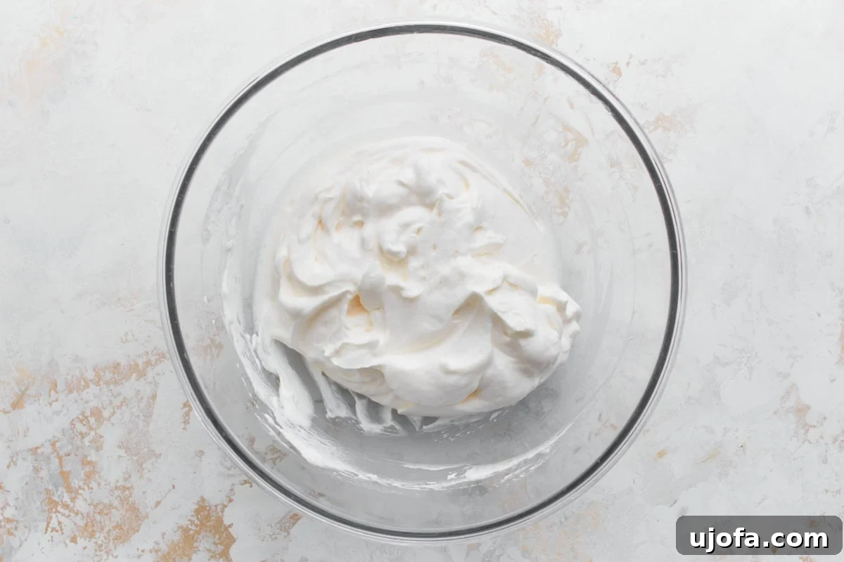 Divine Fruit Ambrosia 5 A clear glass mixing bowl filled with freshly whipped topping, smooth and fluffy, ready to be used as the base for ambrosia salad. The texture is light and airy, perfect for incorporating other ingredients.