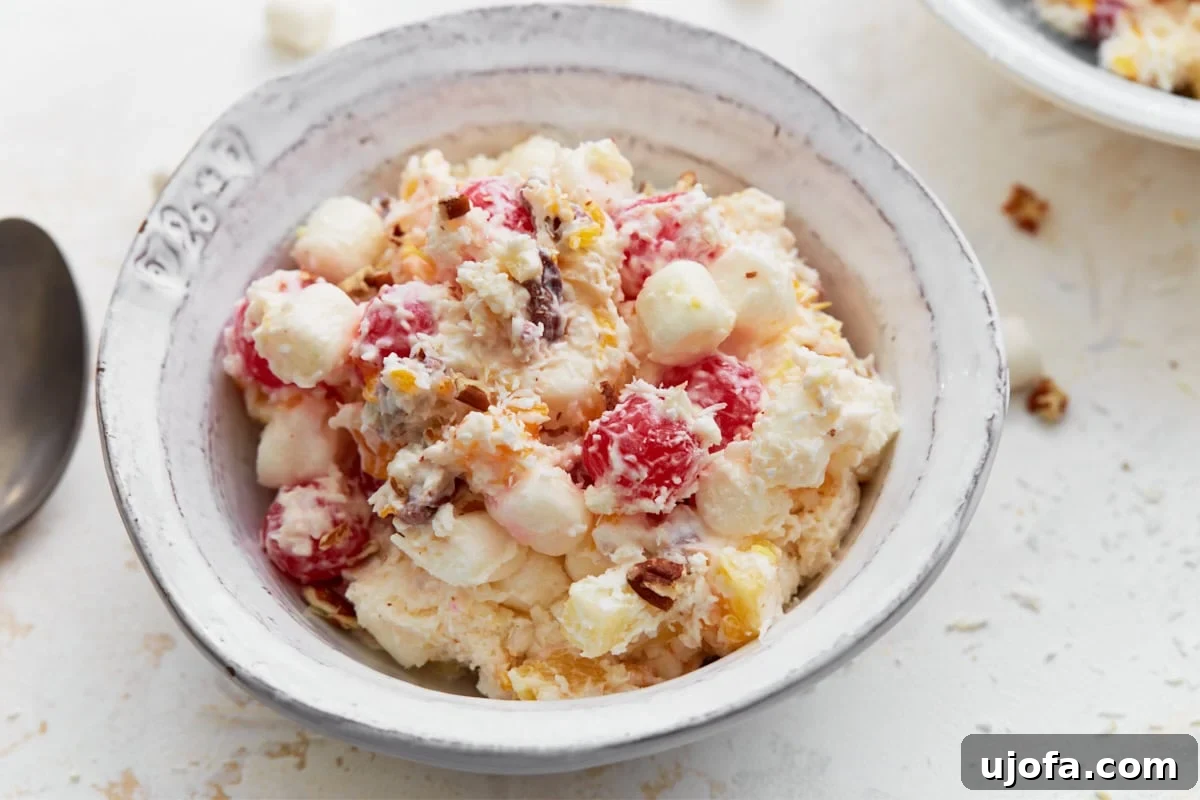Divine Fruit Ambrosia 7 A close-up of a rustic ceramic bowl filled with perfectly chilled ambrosia salad, showcasing the bright red cherries, soft white marshmallows, and golden pineapple pieces, all glistening with the creamy dressing. A few fruit and coconut toppings are artfully scattered around the bowl.