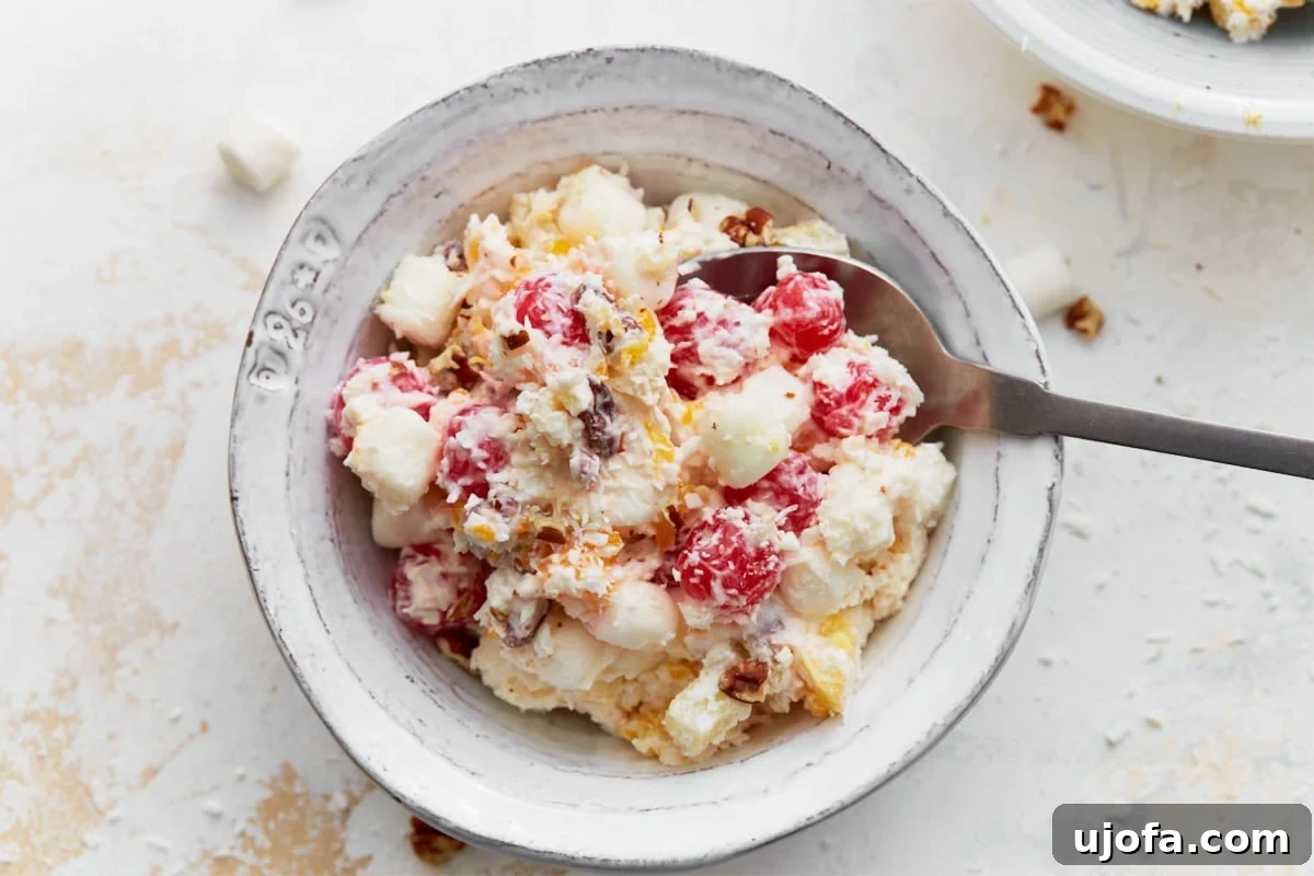 Divine Fruit Ambrosia 8 A beautifully presented bowl of ambrosia salad, with a serving spoon resting inside, inviting one to indulge. The creamy mixture is generously packed with colorful fruit, fluffy marshmallows, and crunchy nuts, creating a perfect balance of texture and vibrant hues, ready for enjoyment.