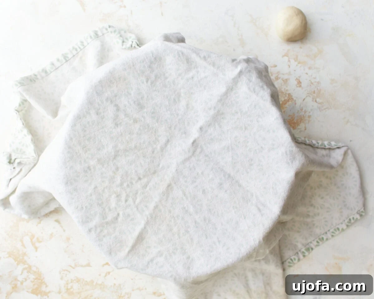 A mixing bowl filled with gluten-free tortilla dough, carefully covered with a clean kitchen towel to maintain moisture and prevent drying.