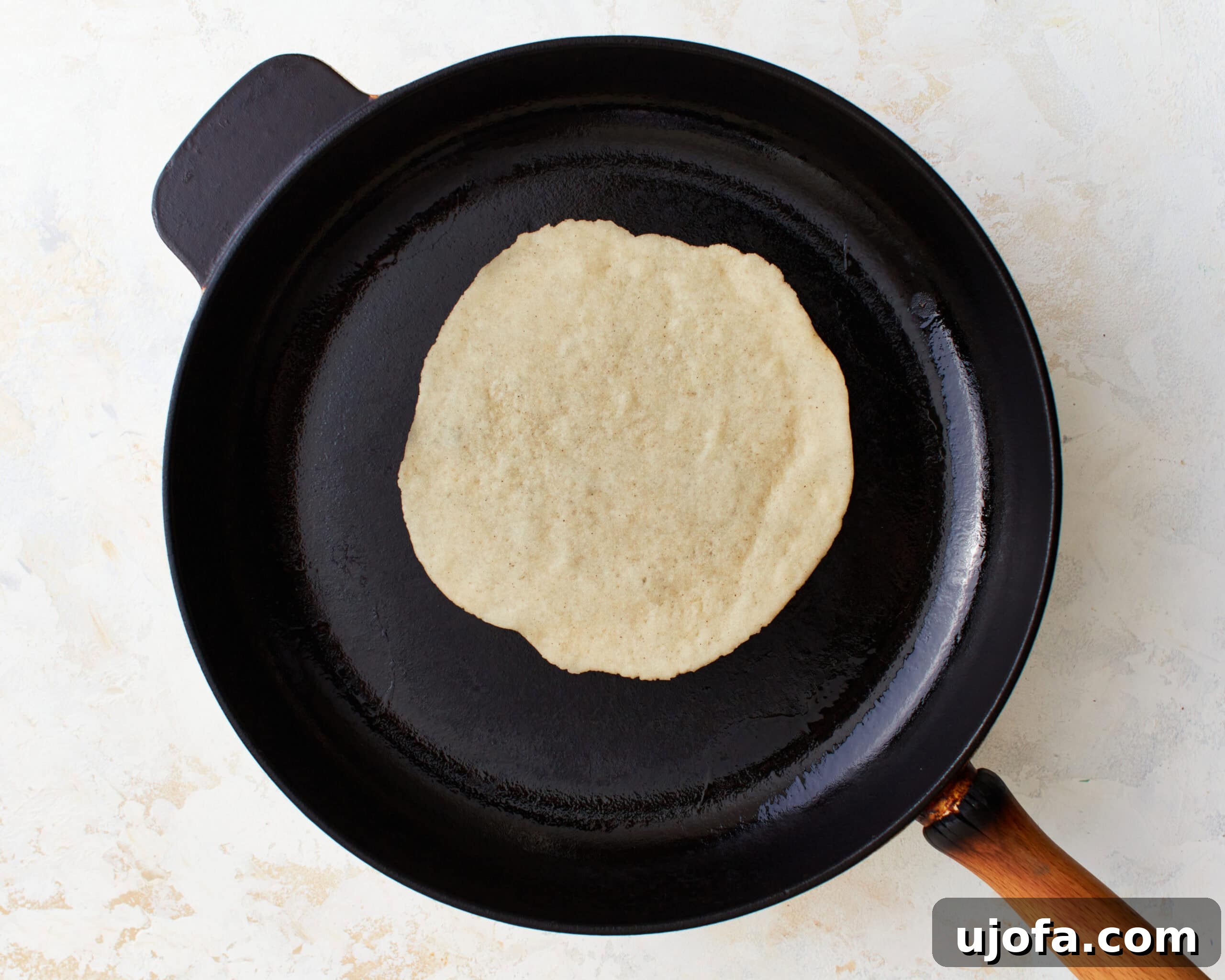 A gluten-free tortilla cooking in a hot, lightly greased cast-iron skillet, showing light browning and slight bubbling on the surface.
