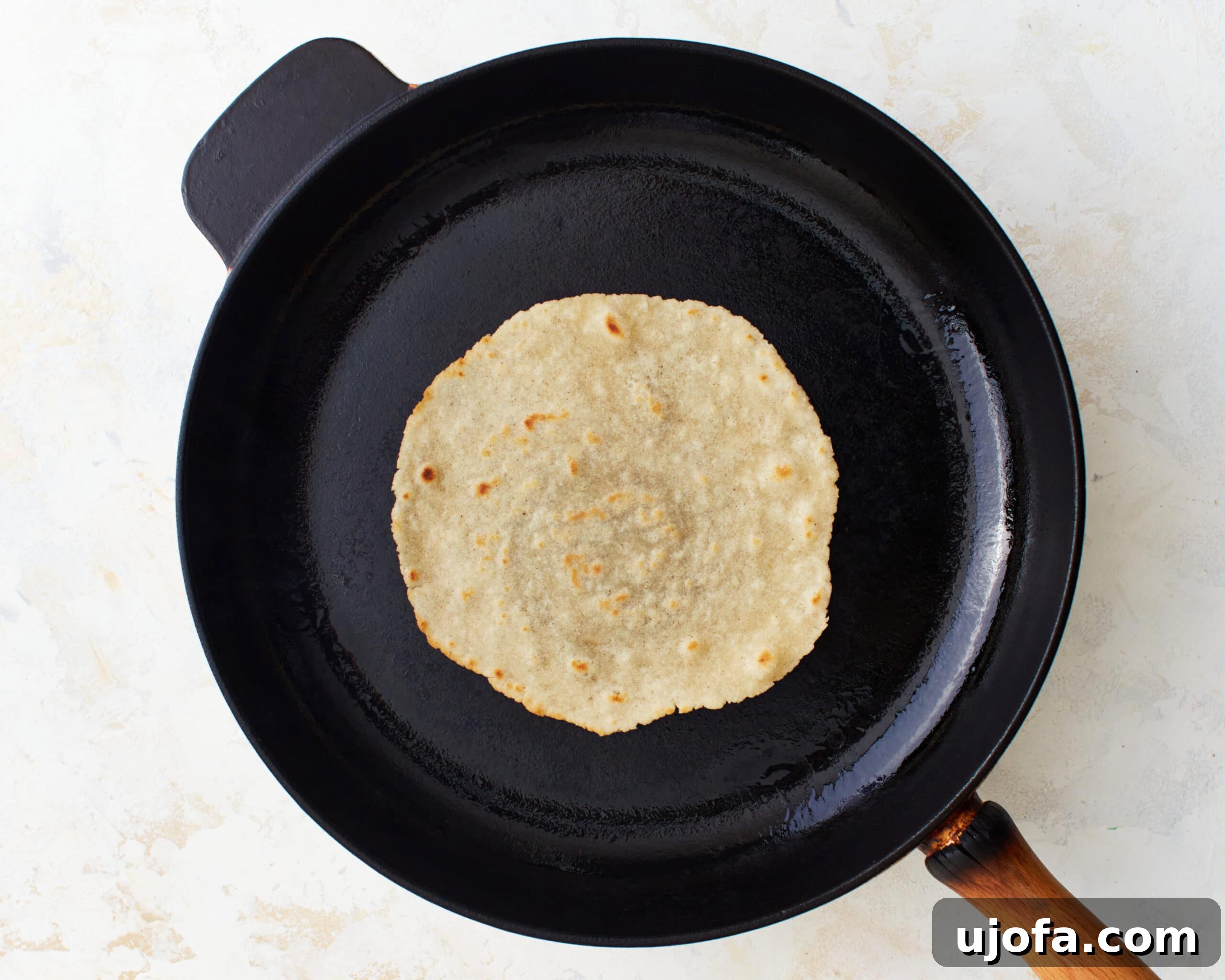 A gluten-free tortilla cooking in a skillet after being expertly flipped, displaying perfect golden-brown spots and a soft texture.
