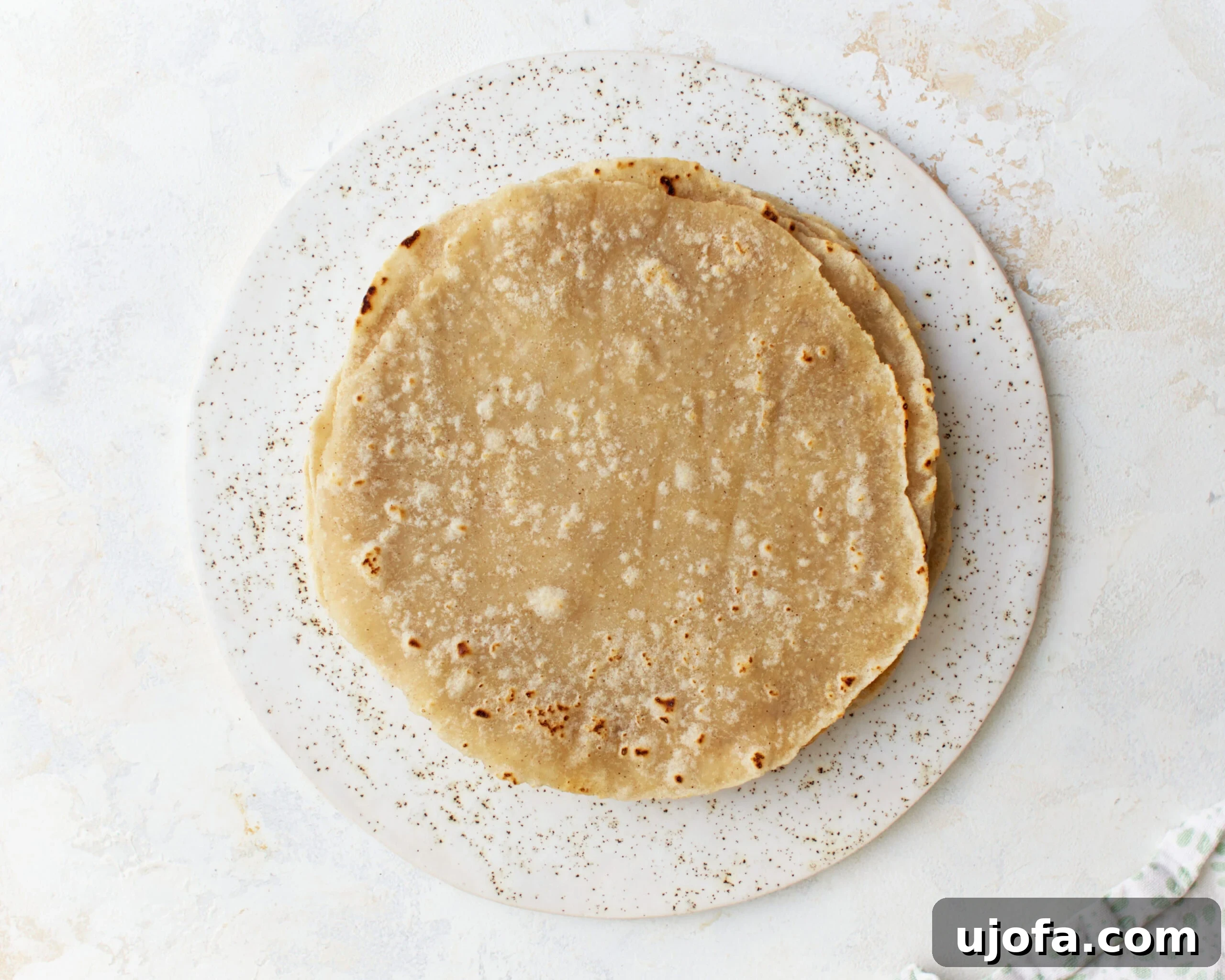 A perfectly stacked pile of freshly cooked gluten-free tortillas on a plate, covered with a kitchen towel to keep them warm and soft until serving.