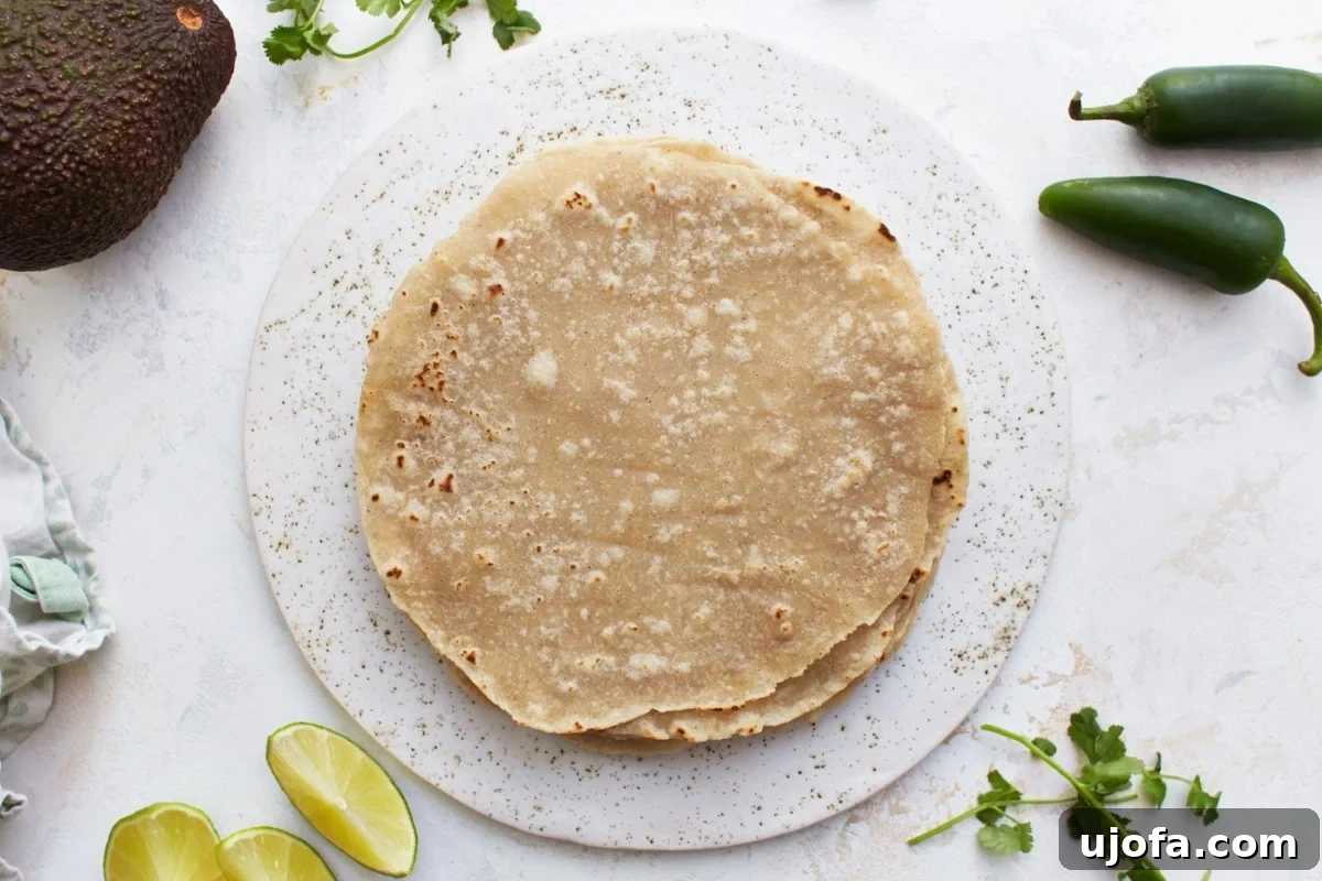 Warm gluten-free flour tortillas beautifully arranged on a white plate, accompanied by fresh avocado slices, vibrant jalapeños, zesty lime wedges, and aromatic cilantro sprigs, showcasing their versatility.