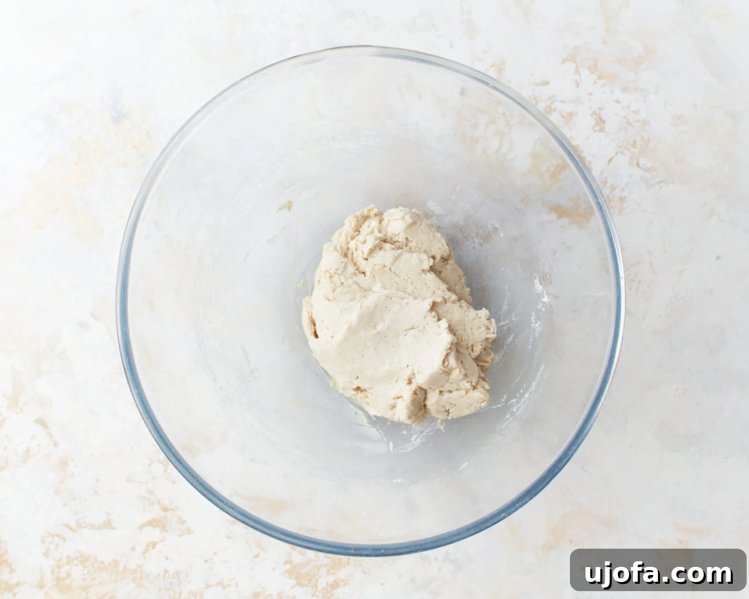 The process of mixing gluten-free tortilla dough begins as warm water and vegetable oil are stirred into the dry flour mixture in a glass bowl.