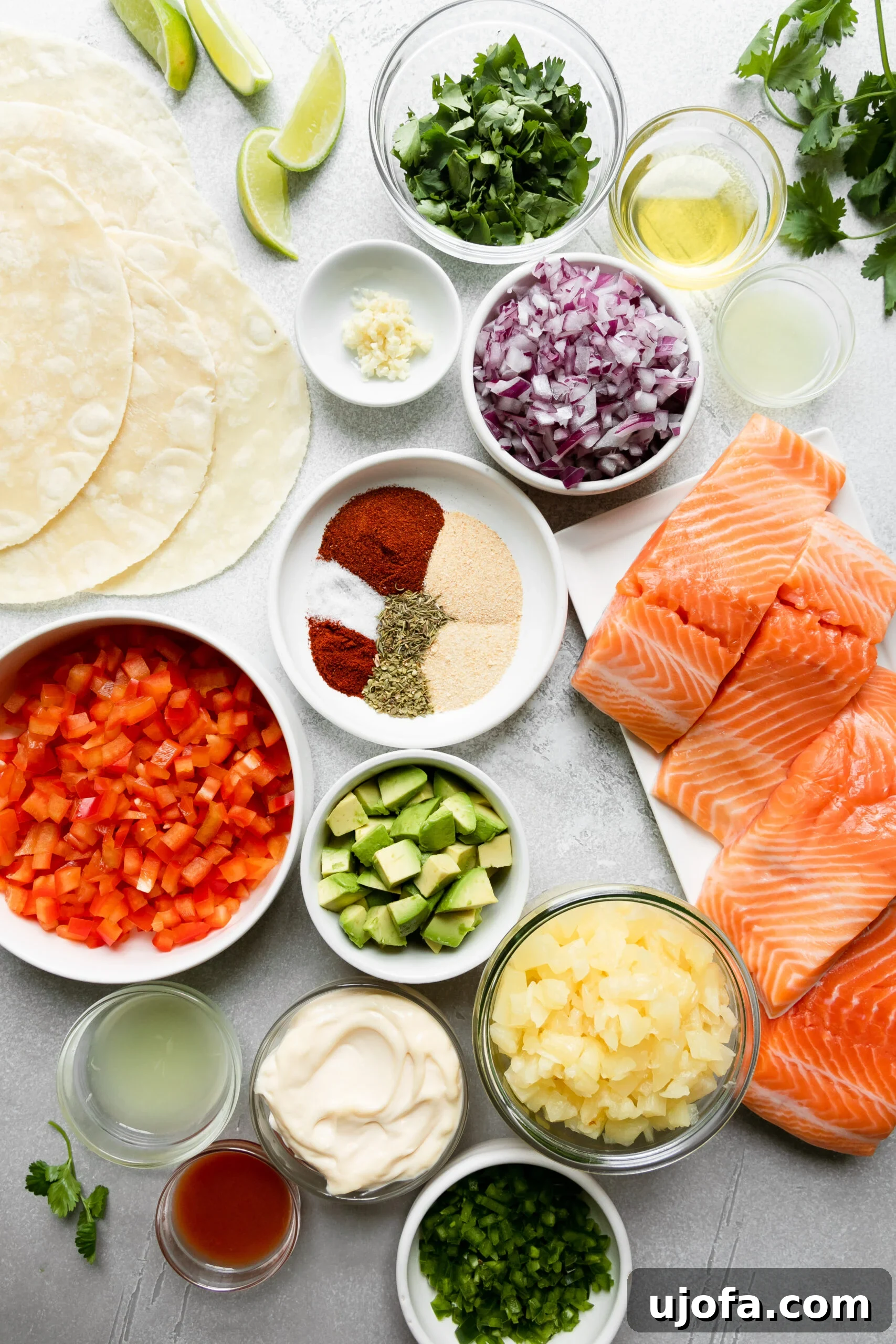 Glass bowls filled with fresh ingredients for pineapple salsa and spicy lime aioli, alongside vibrant lime wedges and gluten-free tortillas, all prepped for making blackened salmon tacos.