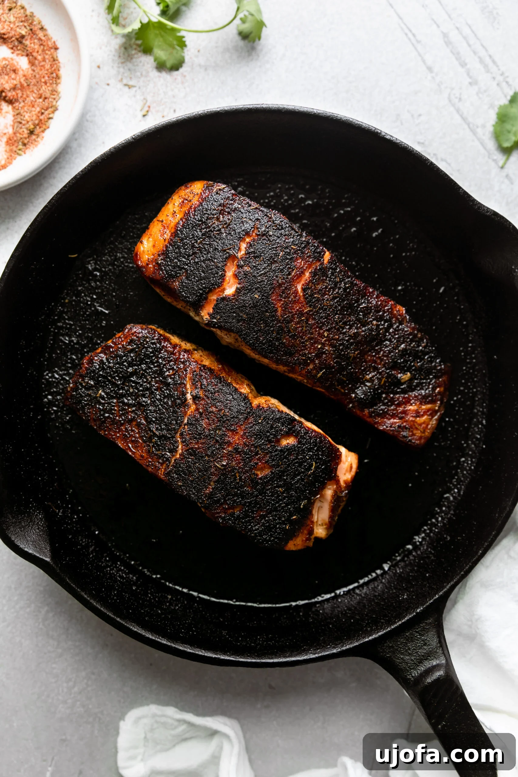 A cast-iron skillet with two pieces of salmon, beautifully blackened with a rich crust, cooking evenly.