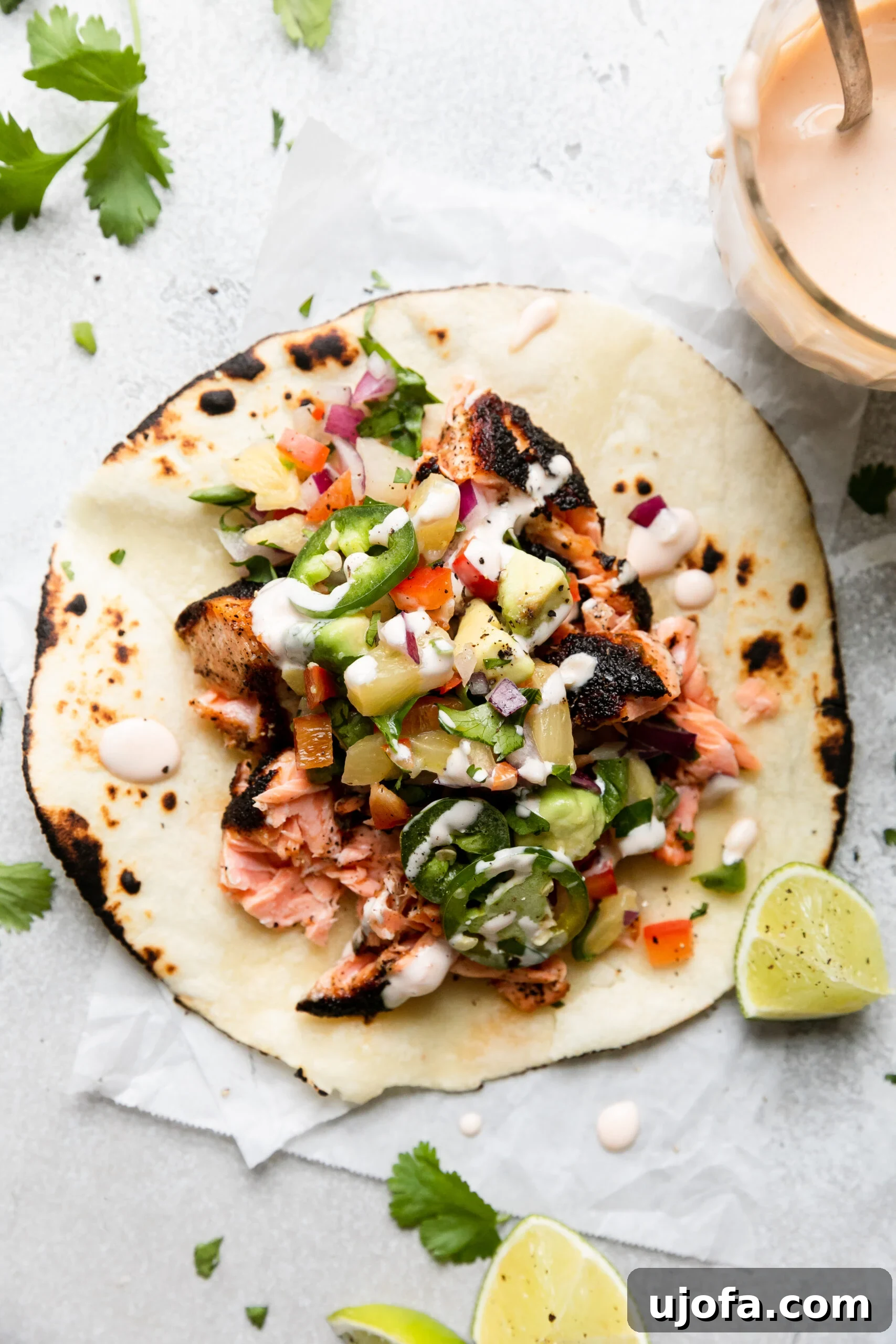 A close-up view of a single gluten-free tortilla generously filled with flaky blackened salmon, vibrant pineapple salsa, and topped with a creamy drizzle of spicy lime aioli.