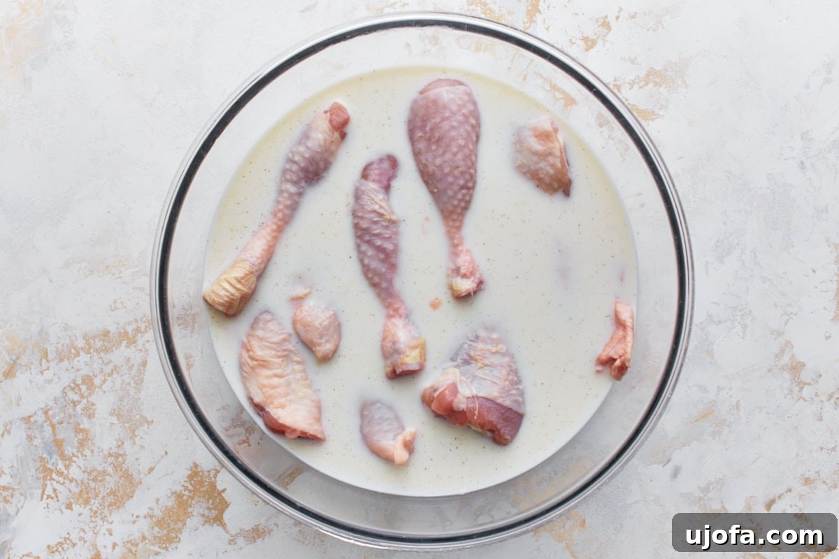 Raw chicken drumsticks and thighs marinating in buttermilk in a large glass bowl