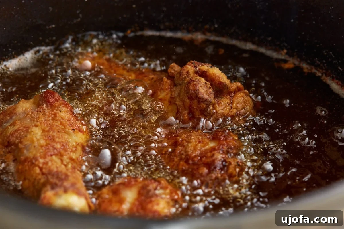 Gluten-free fried chicken frying to golden brown in bubbling frying oil in a cast iron skillet.