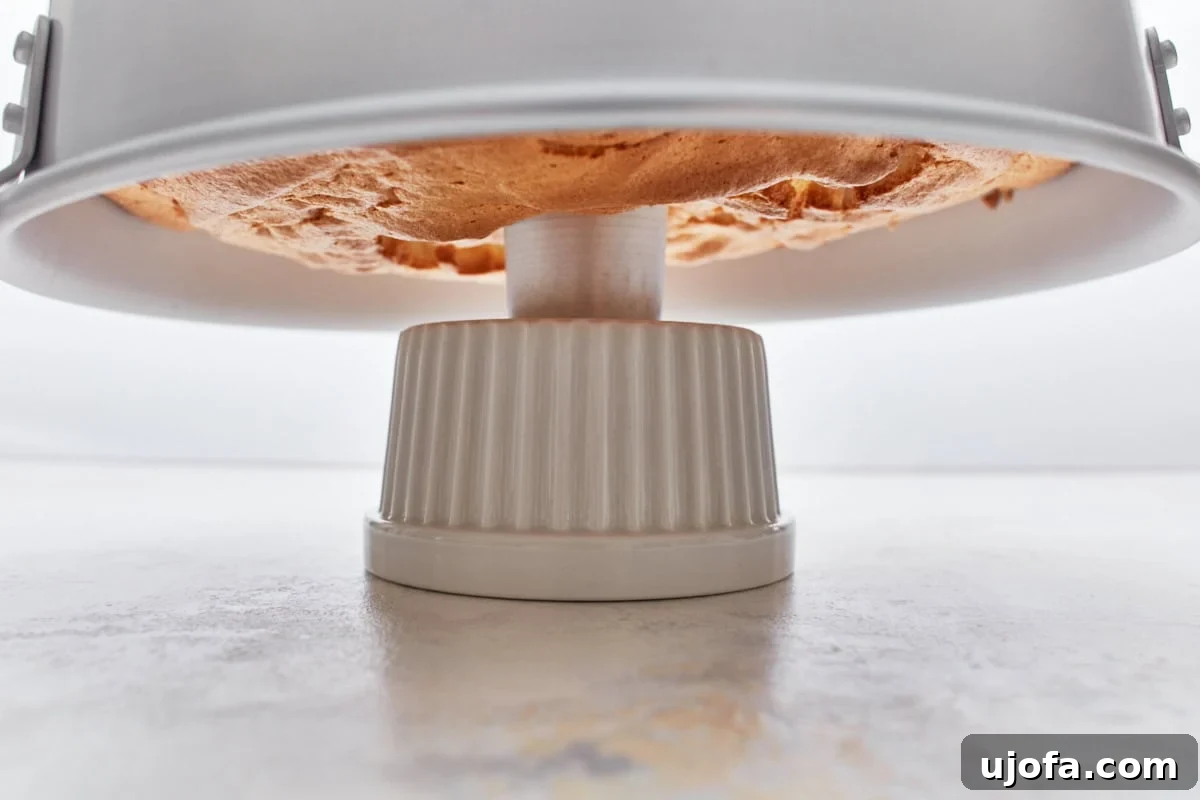 Gluten-free angel food cake in a tube pan cooling upside down on a ceramic holder to prevent collapse.