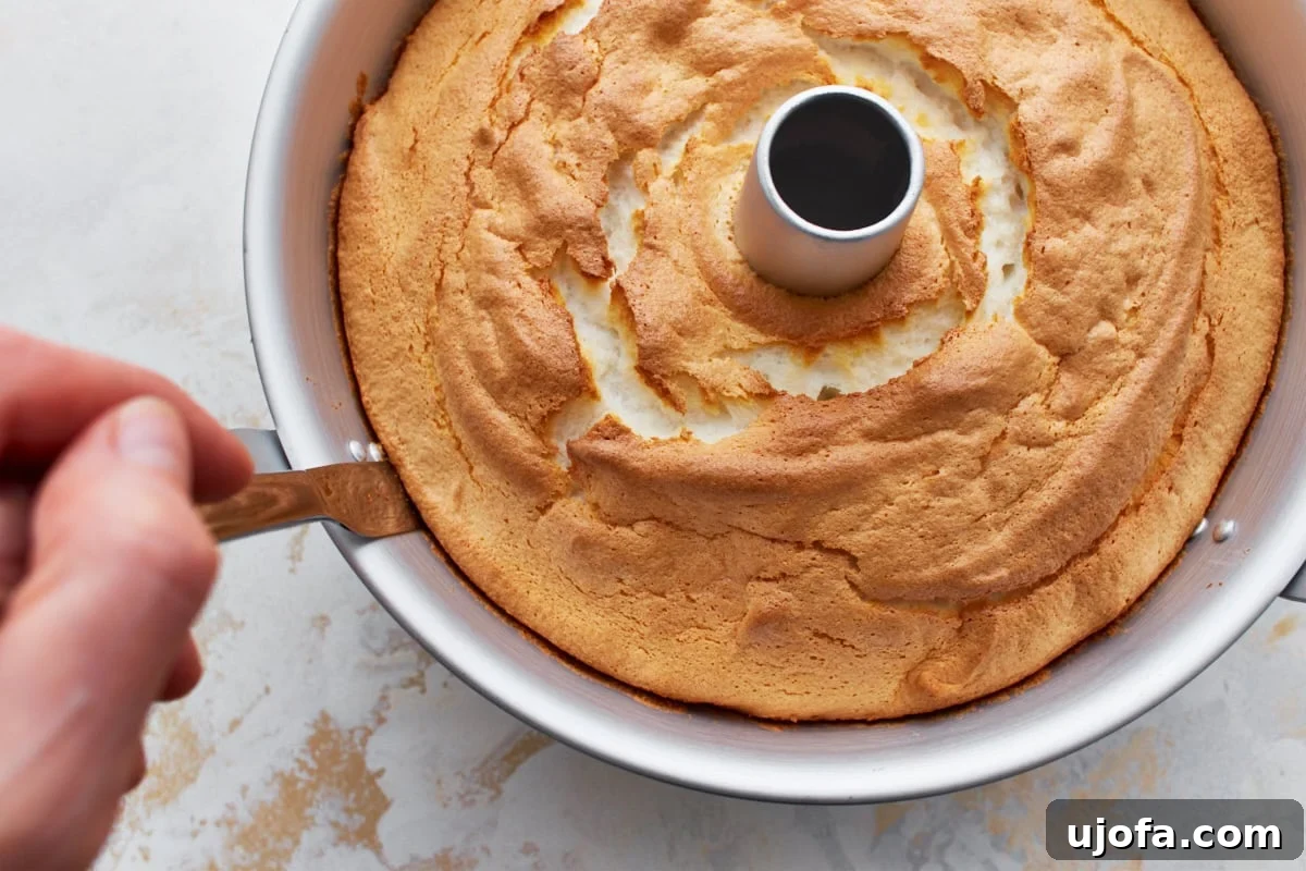 A hand gently loosening the edges of a cooled gluten-free angel food cake from the tube pan using a butter knife.