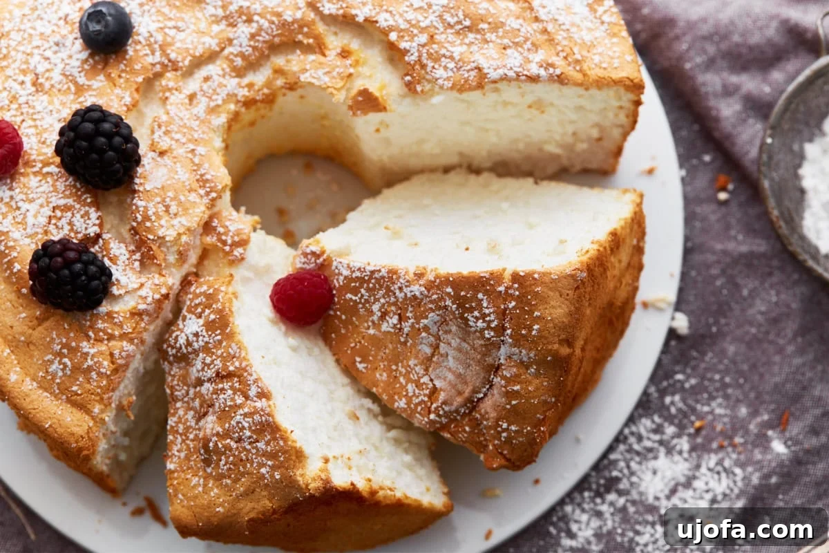 Gluten-free angel food cake with two slices cut and resting on their sides, garnished with powdered sugar and fresh berries.