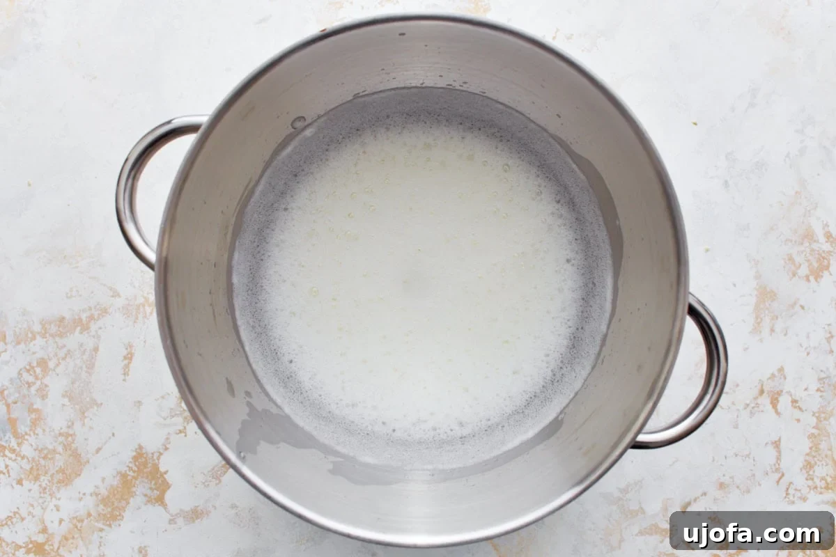 Egg whites and cream of tartar being beaten in a stainless steel mixing bowl.