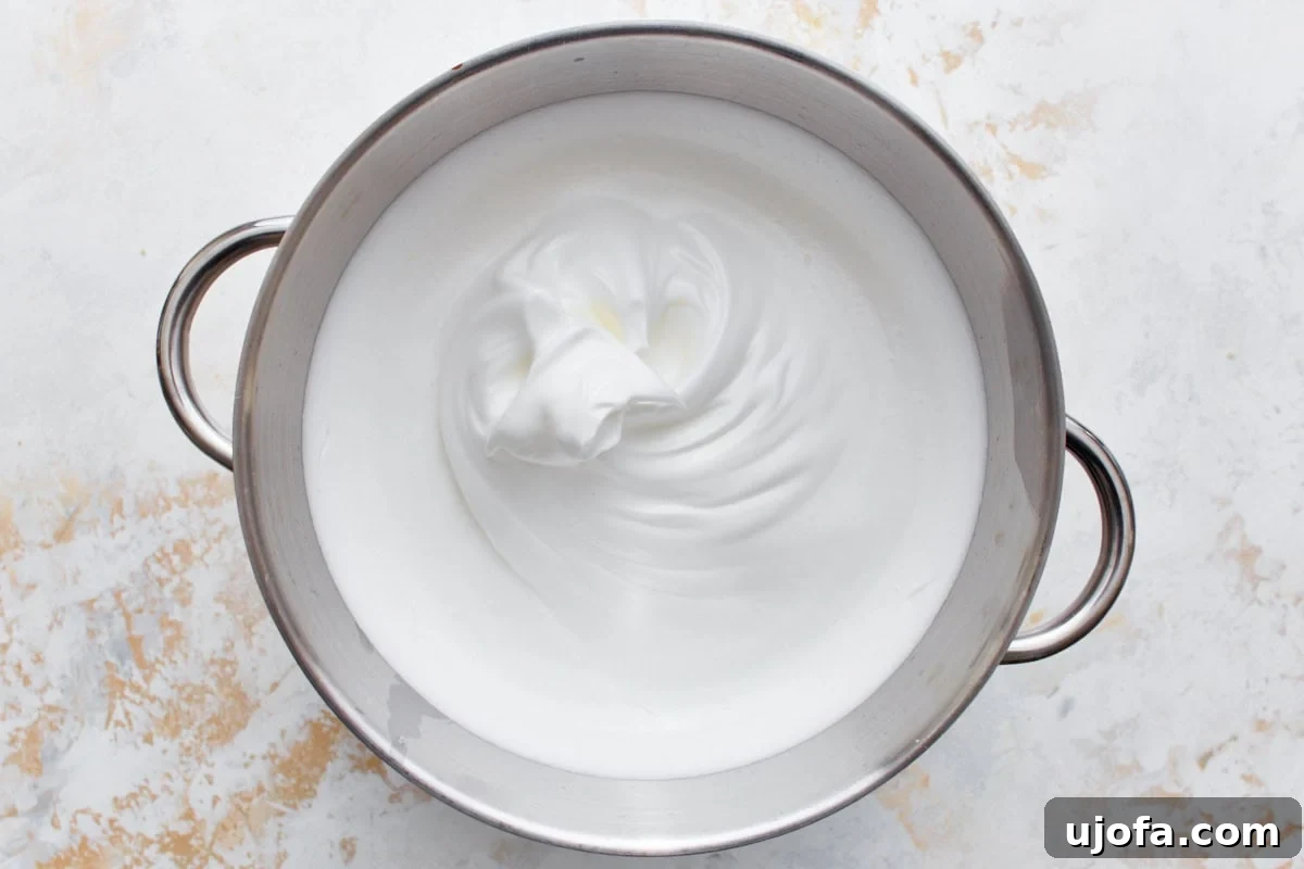 A stainless steel mixing bowl containing perfectly whipped egg white meringue.