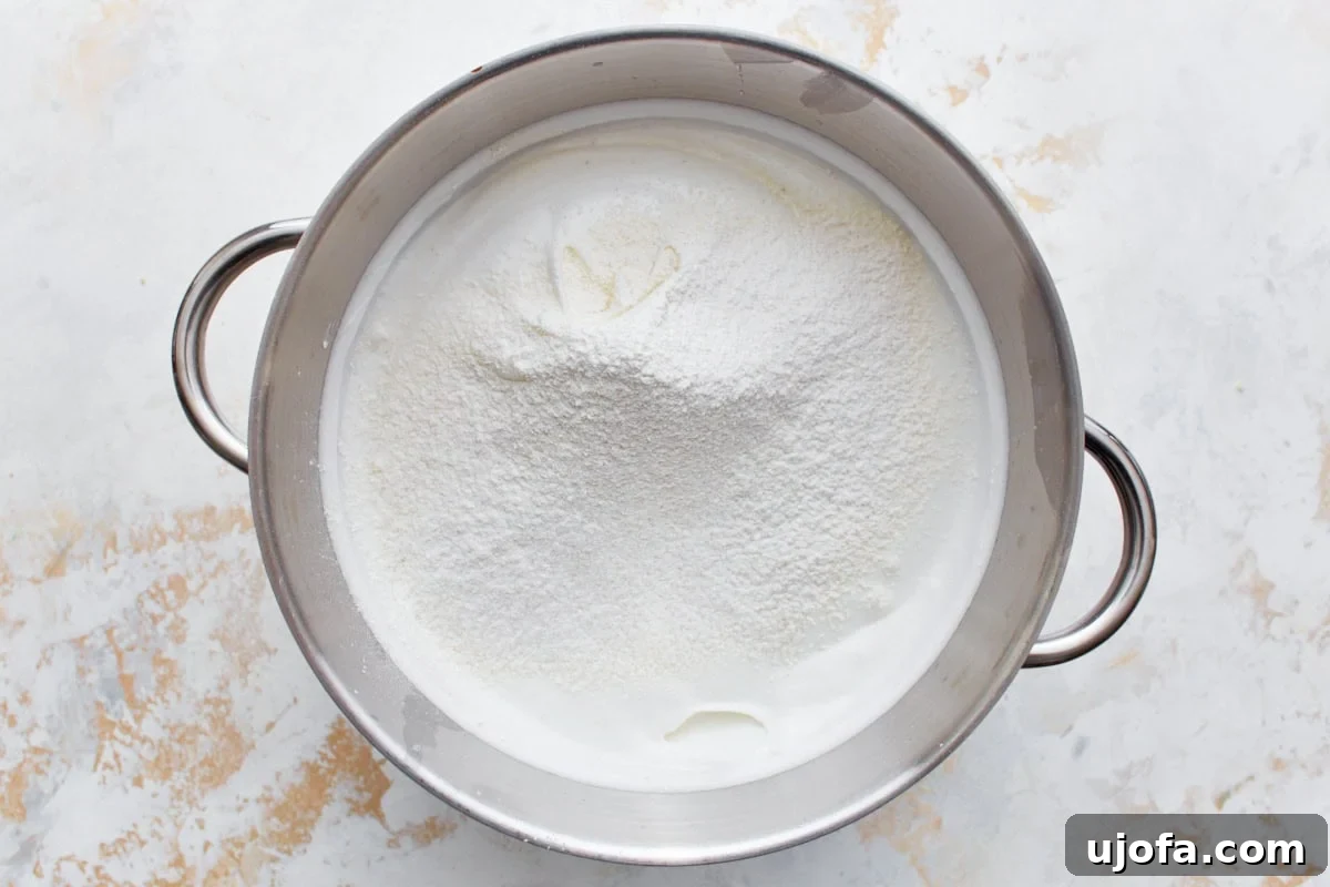 Gluten-free flour mixture gently sprinkled over the whipped egg white meringue in a stainless steel mixing bowl.