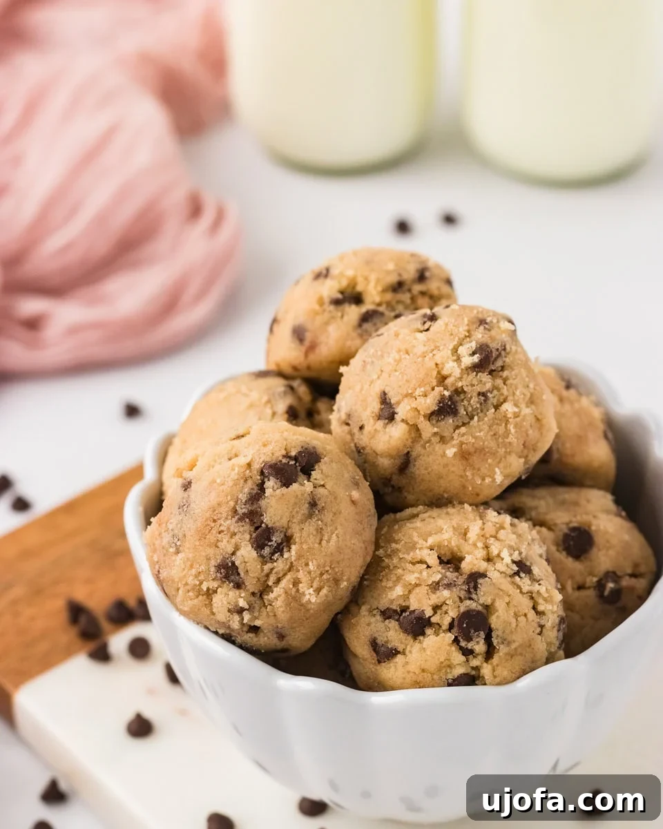 Guilt-Free Gluten-Free Cookie Dough 2 Bowl filled with scoops of gluten-free edible chocolate chip cookie dough, surrounded by scattered mini chocolate chips and glasses of milk in the background. A perfect no-bake dessert for any occasion.