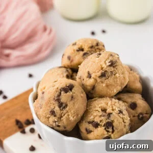 Bowl filled with scoops of gluten-free edible chocolate chip cookie dough, surrounded by scattered mini chocolate chips and glasses of milk in the background.
