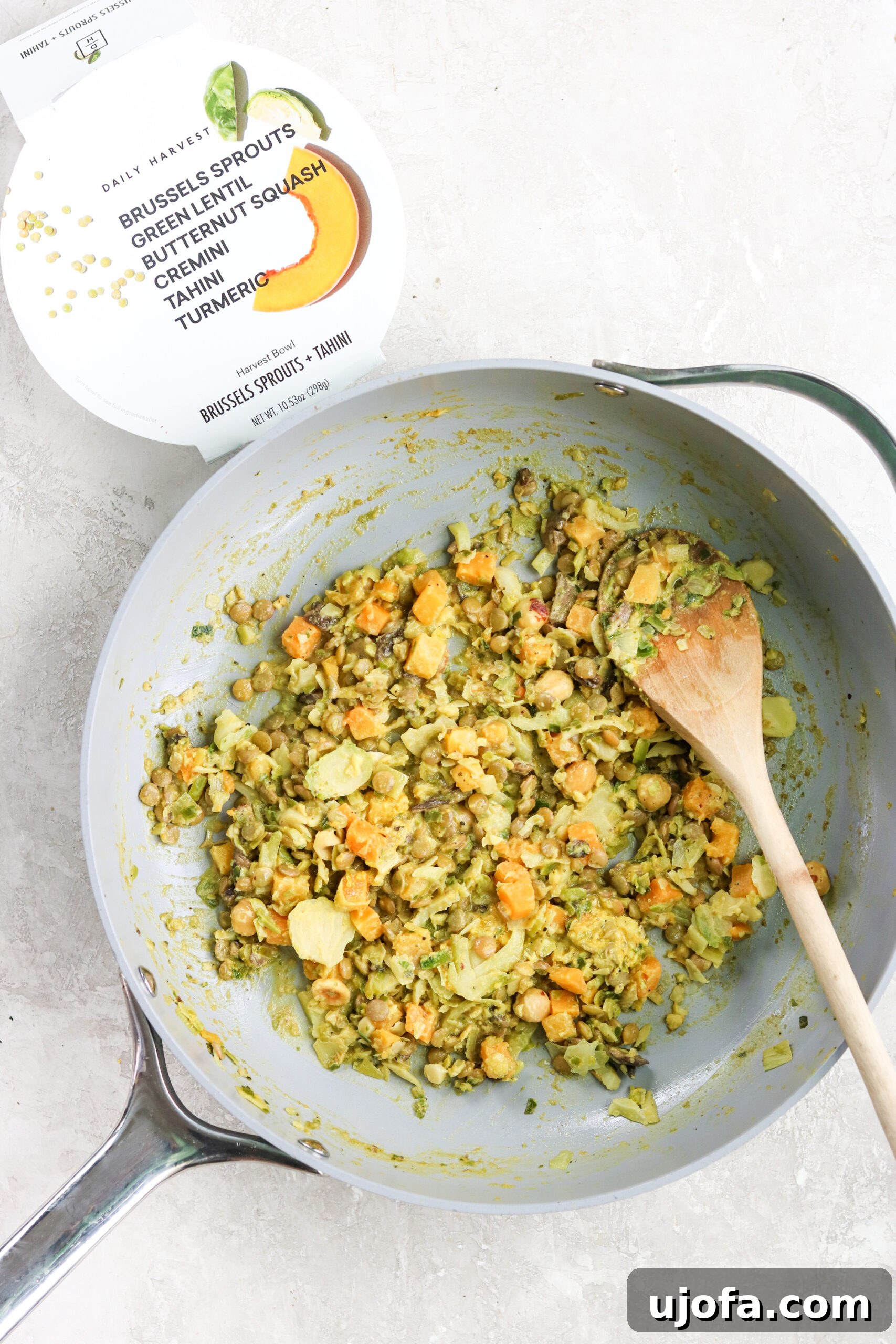 A Daily Harvest Brussels Sprouts & Tahini bowl being expertly prepared in a skillet with a wooden spoon, steam gently rising.