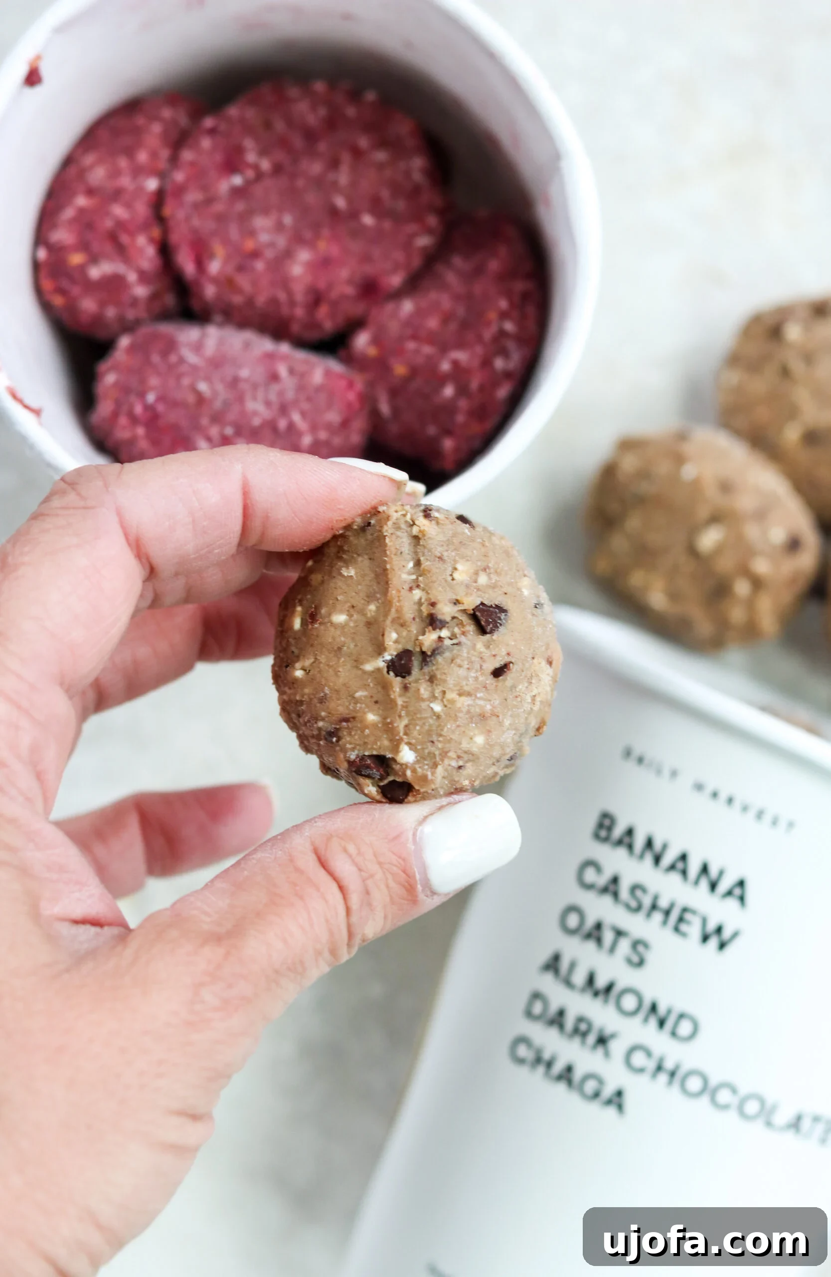 A Daily Harvest Banana and Cacao Bite is held up, with more delicious bites visible in the background, ready to be enjoyed.