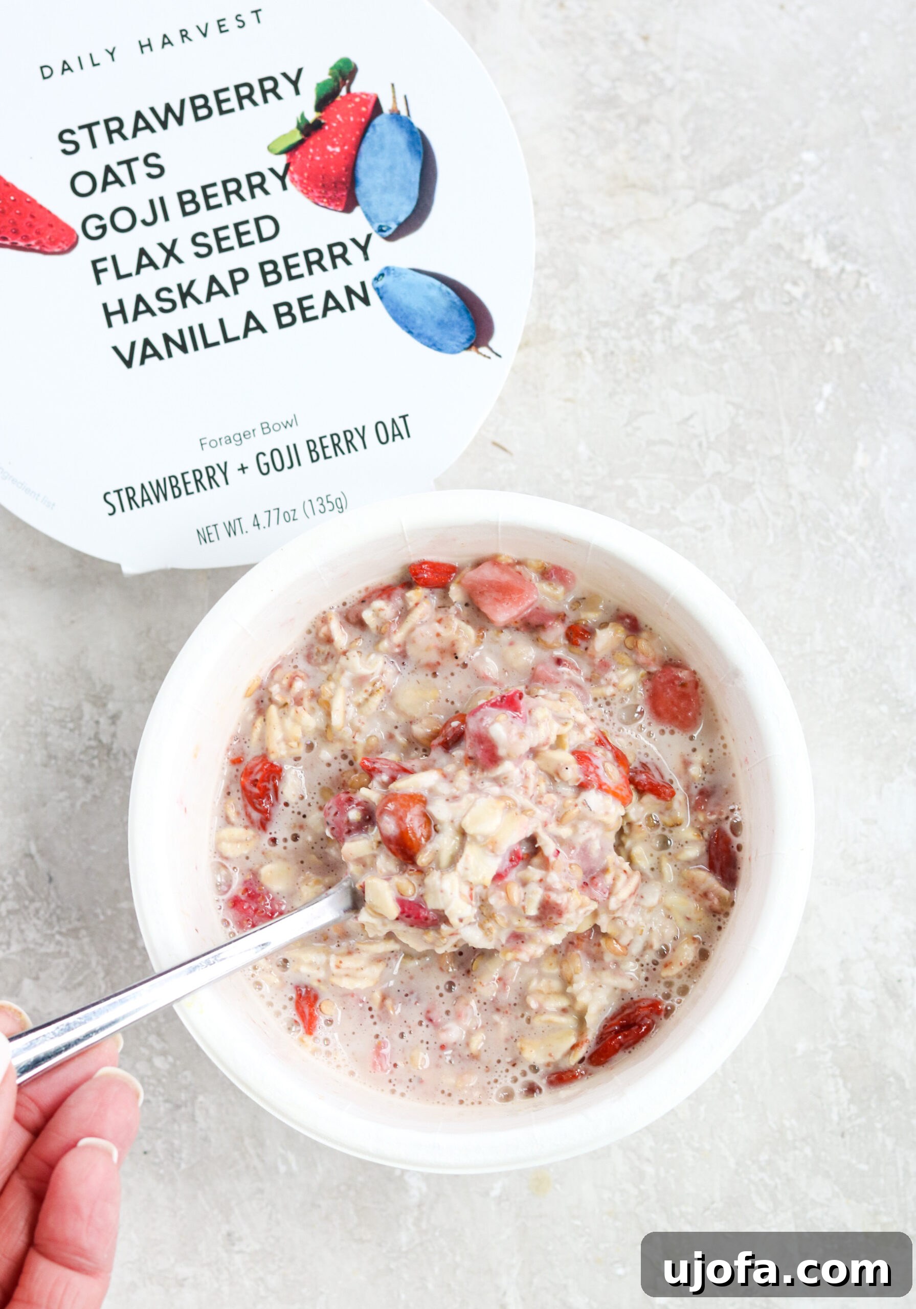 A Daily Harvest Strawberry + Goji Berry Oat bowl mixed with almond milk, ready to eat, with its descriptive lid next to it.