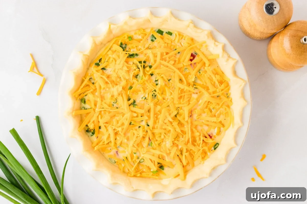 Ultimate Gluten-Free Quiche 10 The prepared gluten-free quiche, with a generous final layer of shredded cheddar cheese sprinkled over the egg mixture and fillings, ready to be baked to golden perfection.