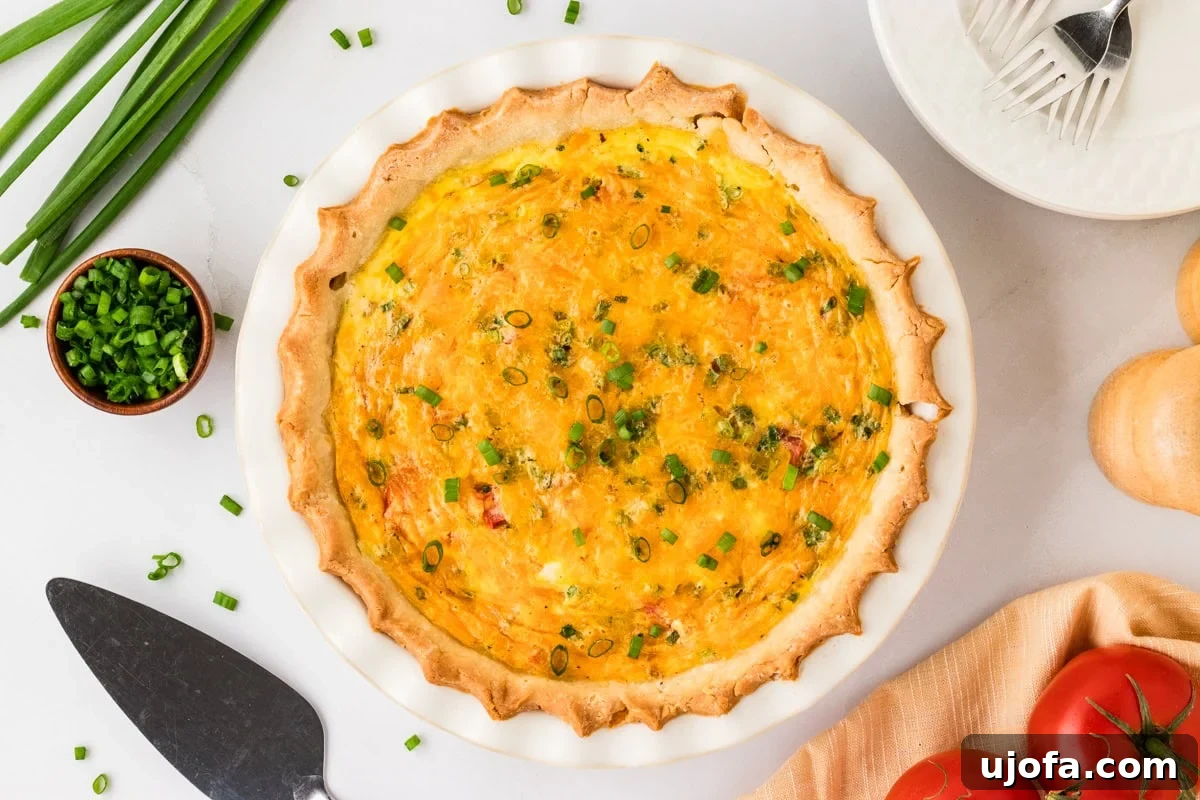 Ultimate Gluten-Free Quiche 11 A freshly baked gluten-free quiche, with a beautiful golden crust and bubbling cheese topping, lightly garnished with green onions. The setting includes fresh tomatoes and green onions around the dish, suggesting a garden-fresh meal.