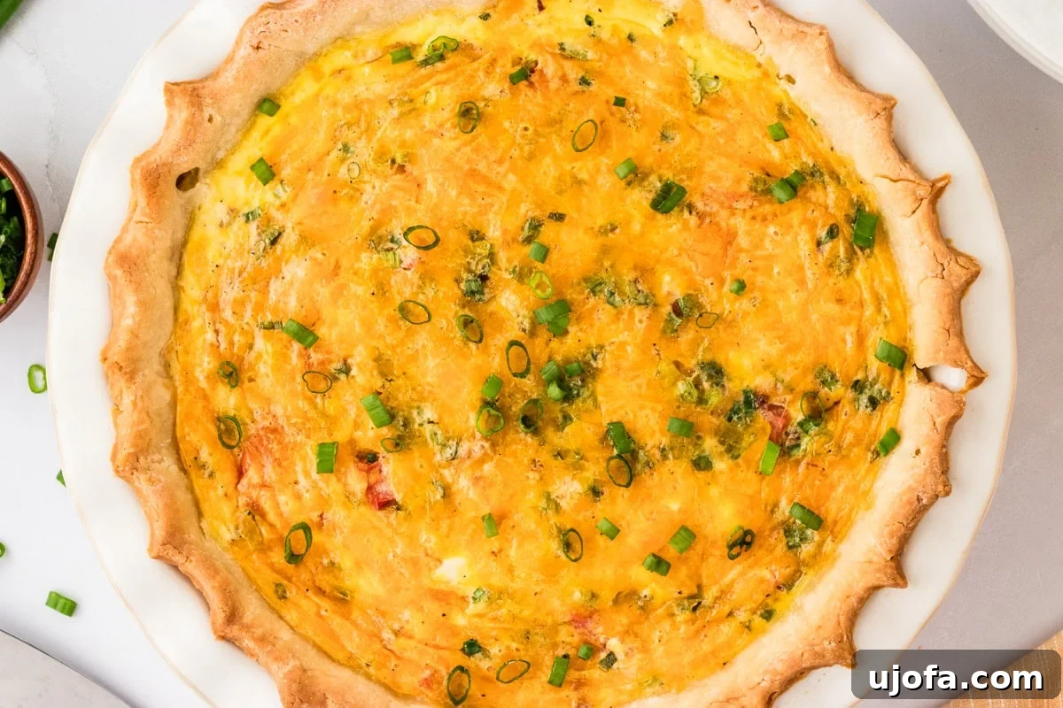 Ultimate Gluten-Free Quiche 12 A close-up, overhead shot of a freshly baked quiche. The golden-brown crust and melted, bubbling cheddar cheese topping are visible, with scattered green onion garnishes adding fresh color.