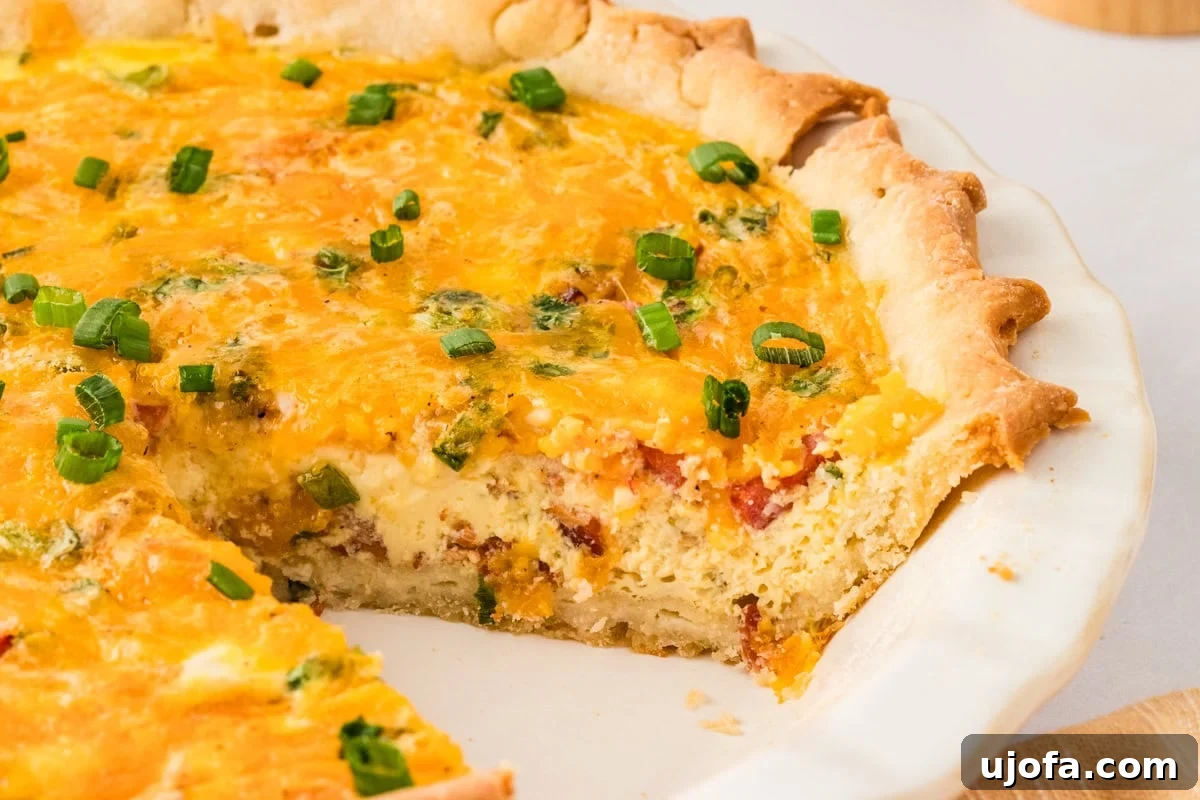 Ultimate Gluten-Free Quiche 13 A baked gluten-free quiche with a slice removed, revealing the rich, creamy filling of eggs, cheese, bacon, and diced tomatoes, all nestled in a flaky crust. Green onions garnish the top.