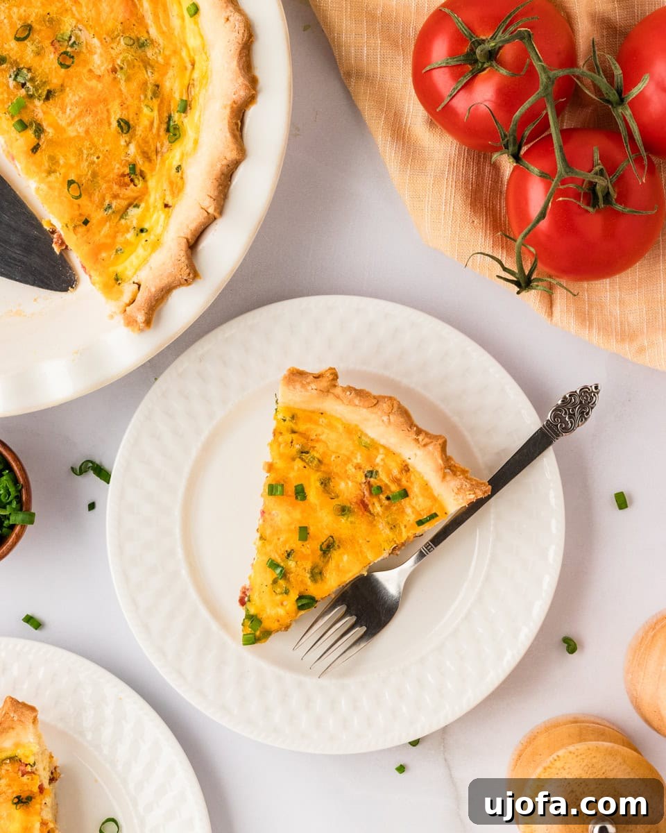 Ultimate Gluten-Free Quiche 15 An overhead view of a perfectly baked gluten-free quiche slice on a white plate, with a fork positioned beside it. The background features fresh tomatoes, green onions, and the remaining whole quiche in its pie dish, creating an inviting culinary scene.