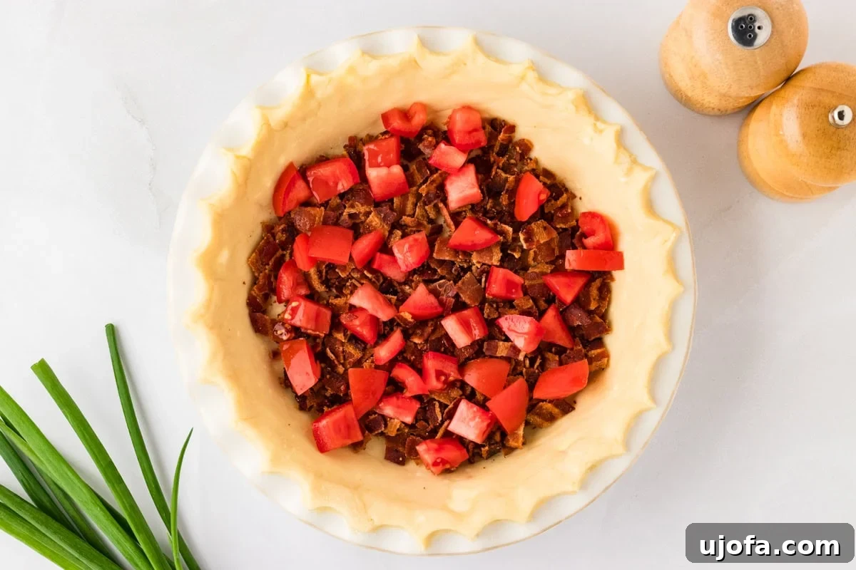 Ultimate Gluten-Free Quiche 7 A prepared gluten-free pie crust in a dish, already filled with a layer of chopped, crumbled bacon and diced red tomatoes, forming a colorful base for the quiche.