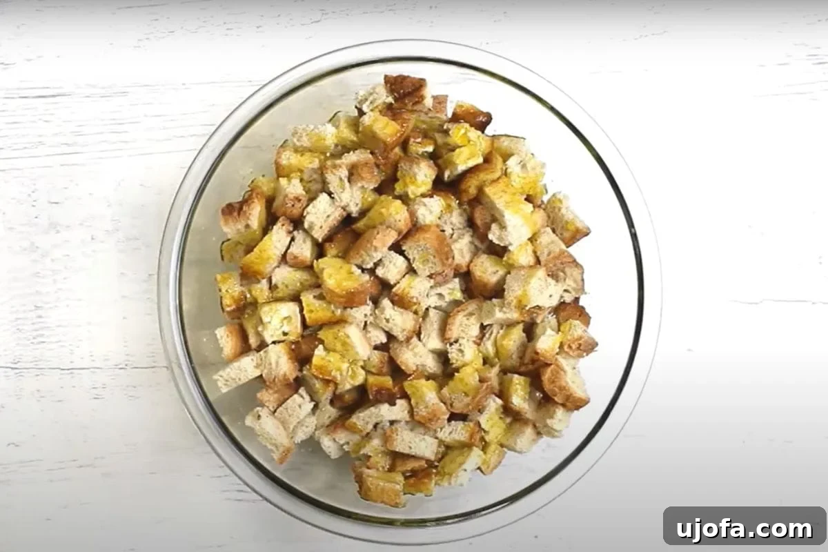 Crafting Delicious Gluten-Free Croutons 7 Gluten-free bread cubes in a clear glass mixing bowl, generously coated with olive oil and a mix of classic seasonings, ready for baking.
