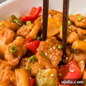 Flavorful Gluten-Free Chicken Feasts 12 Up close view of chopsticks picking up a piece of sweet and sour chicken, highlighting its glossy sauce and tender texture.