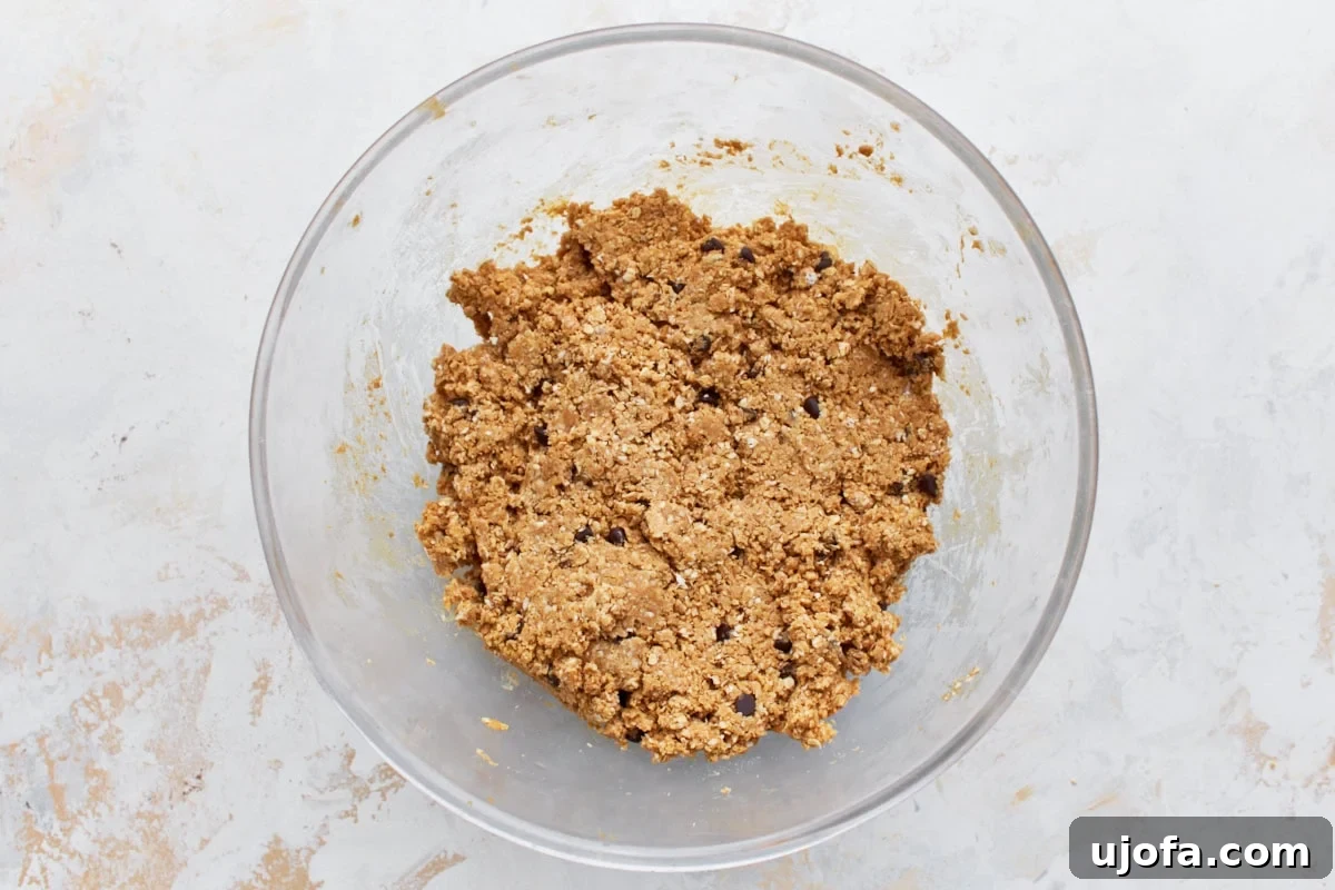 Gluten-free granola bar dough mixed with chocolate chips in a glass bowl, showing the crumbly texture before pressing.