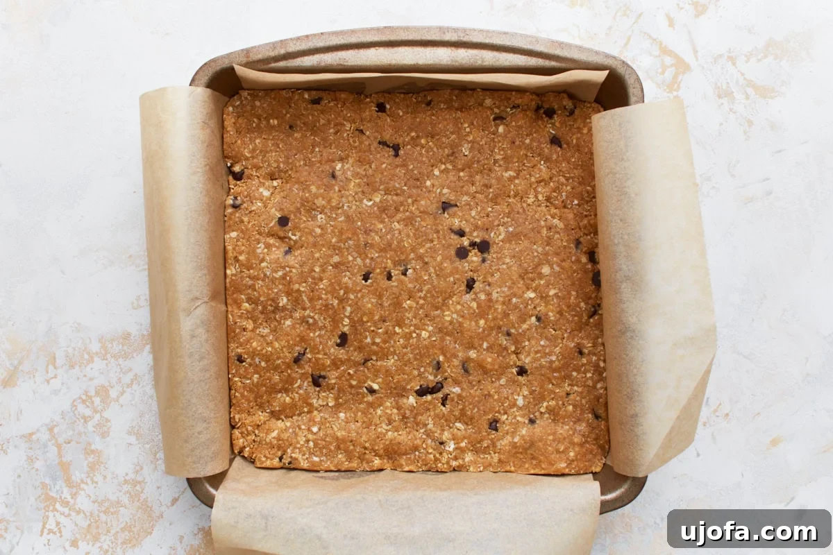 Pressed gluten-free granola bar mixture in a parchment-lined baking dish, flattened and ready for chilling.