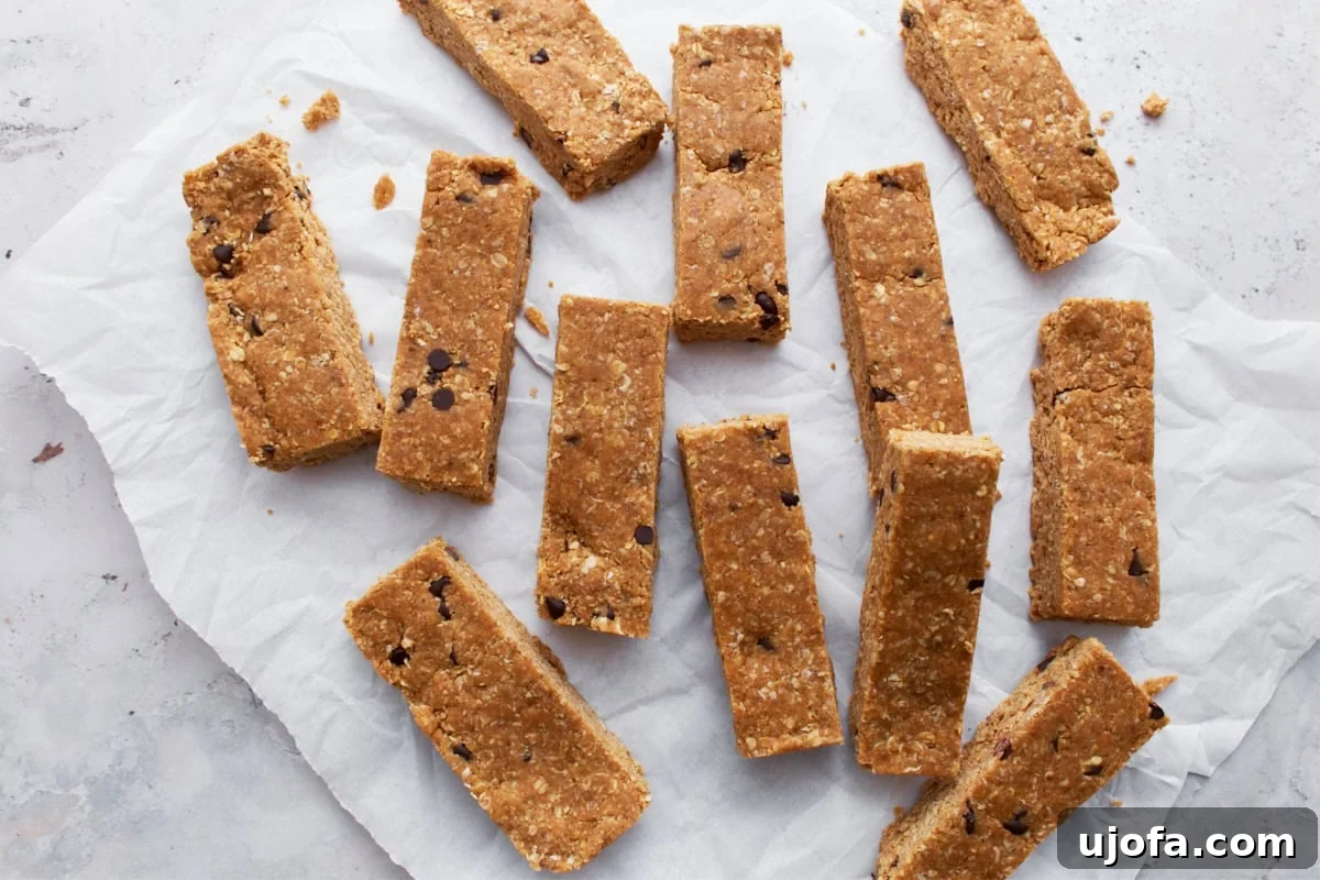 A collection of gluten-free granola bars spread out on parchment paper, highlighting their uniform shape and chocolate chip accents, ready for storage.