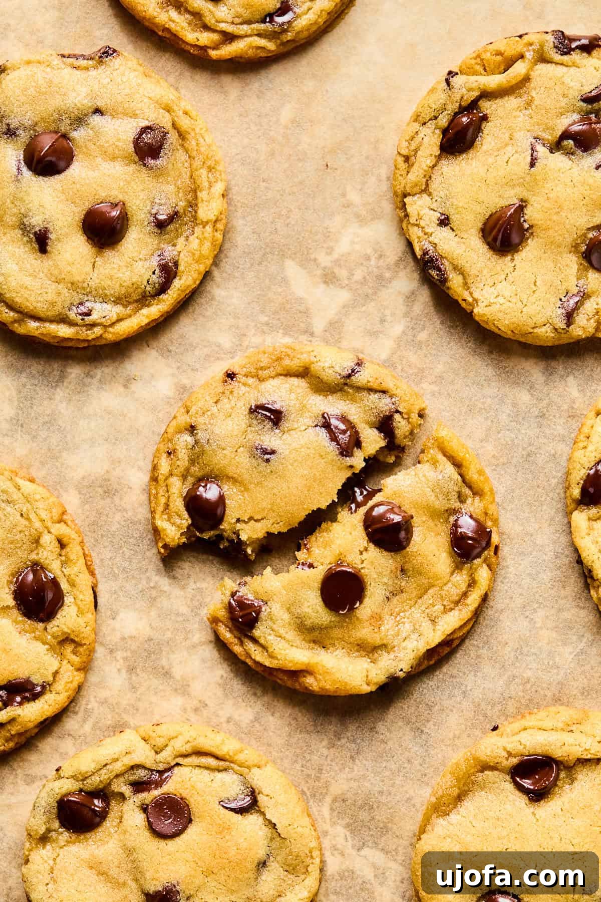 Baked gluten-free chocolate chip cookies on a baking sheet, with one cookie torn in half to show its soft, melty chocolate interior.
