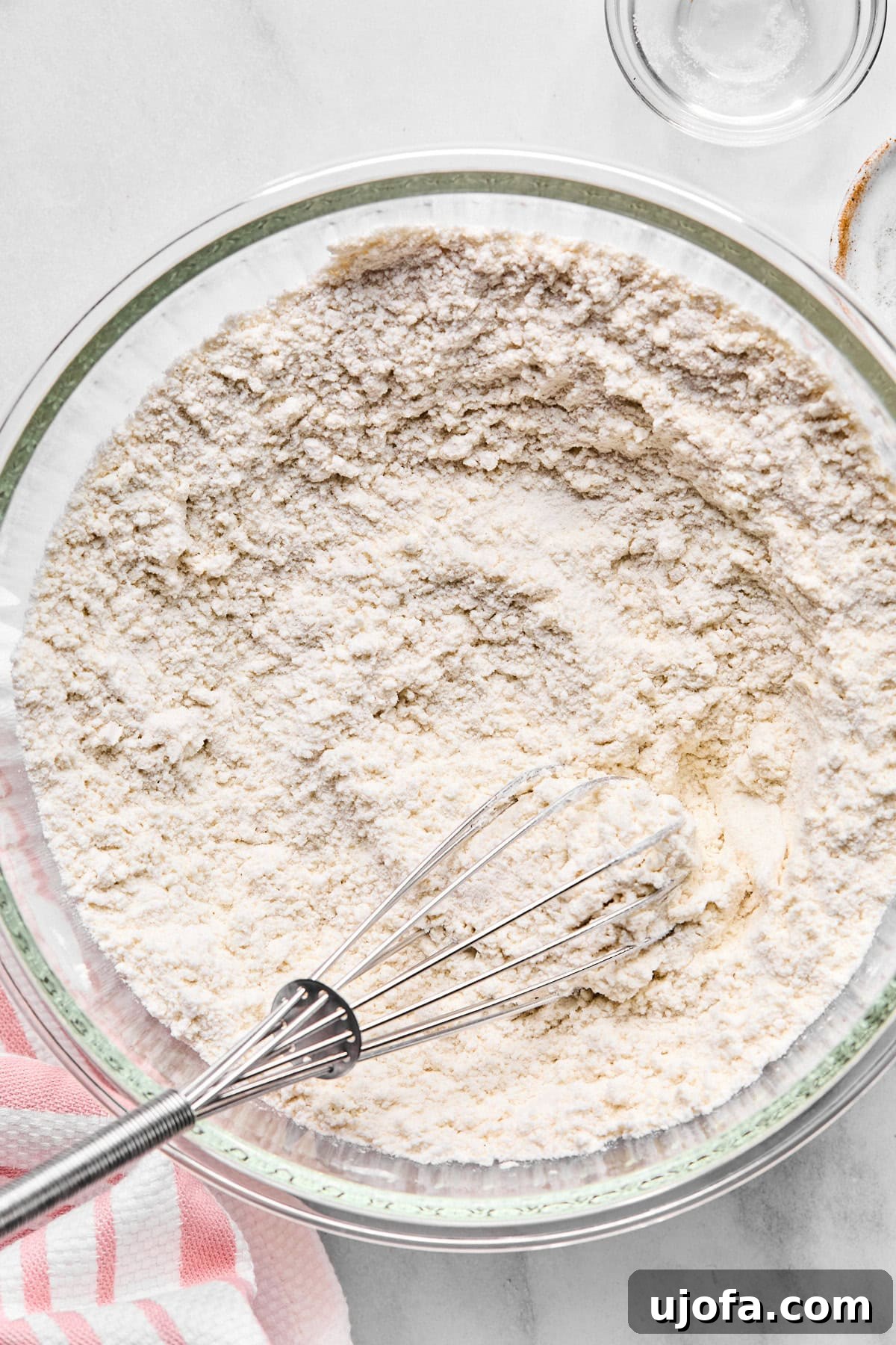 Dry ingredients in a bowl, including gluten-free flour, baking soda, baking powder, and salt, with a whisk.