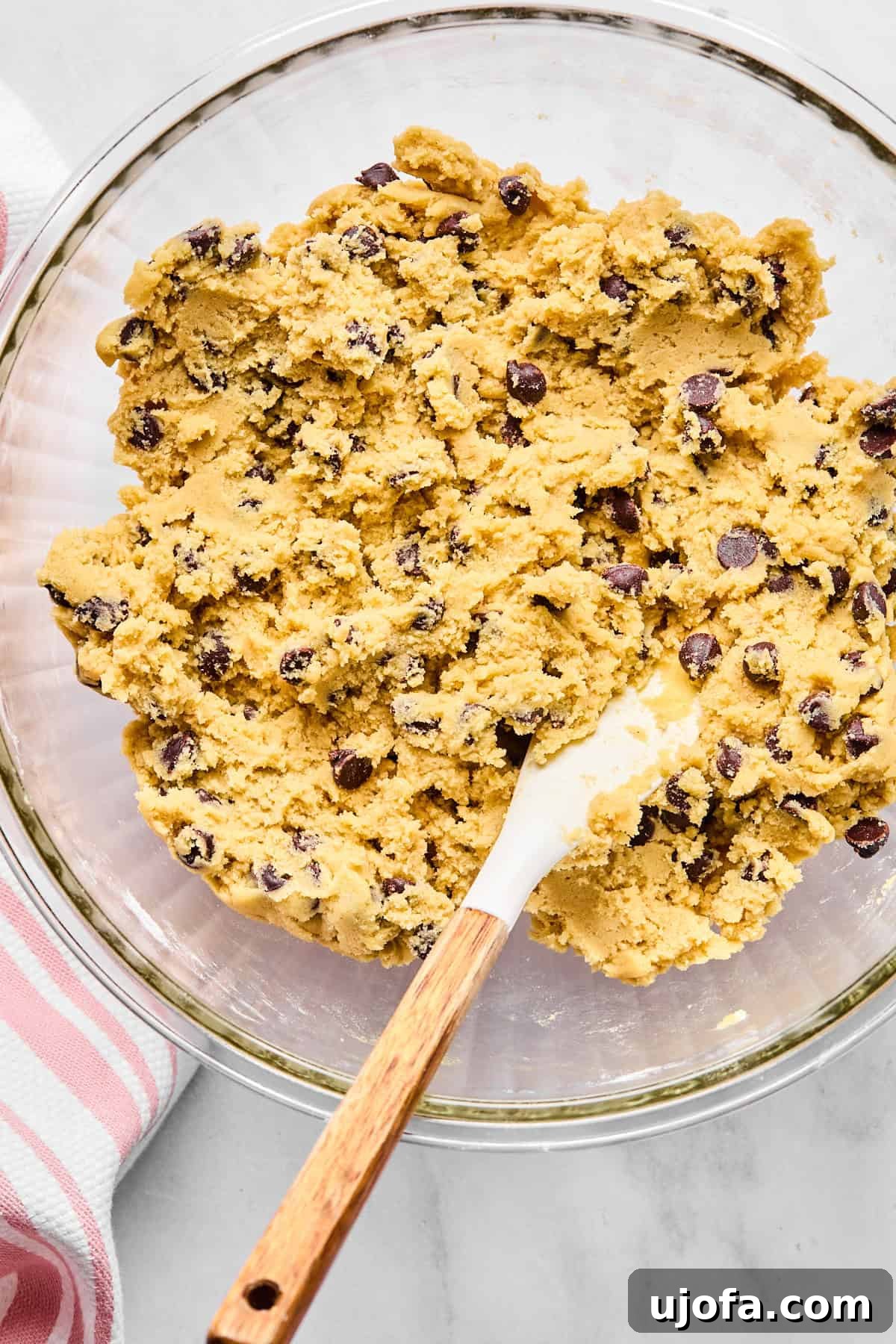 Chocolate chip cookie dough in a glass bowl with a spoon, ready for chilling.