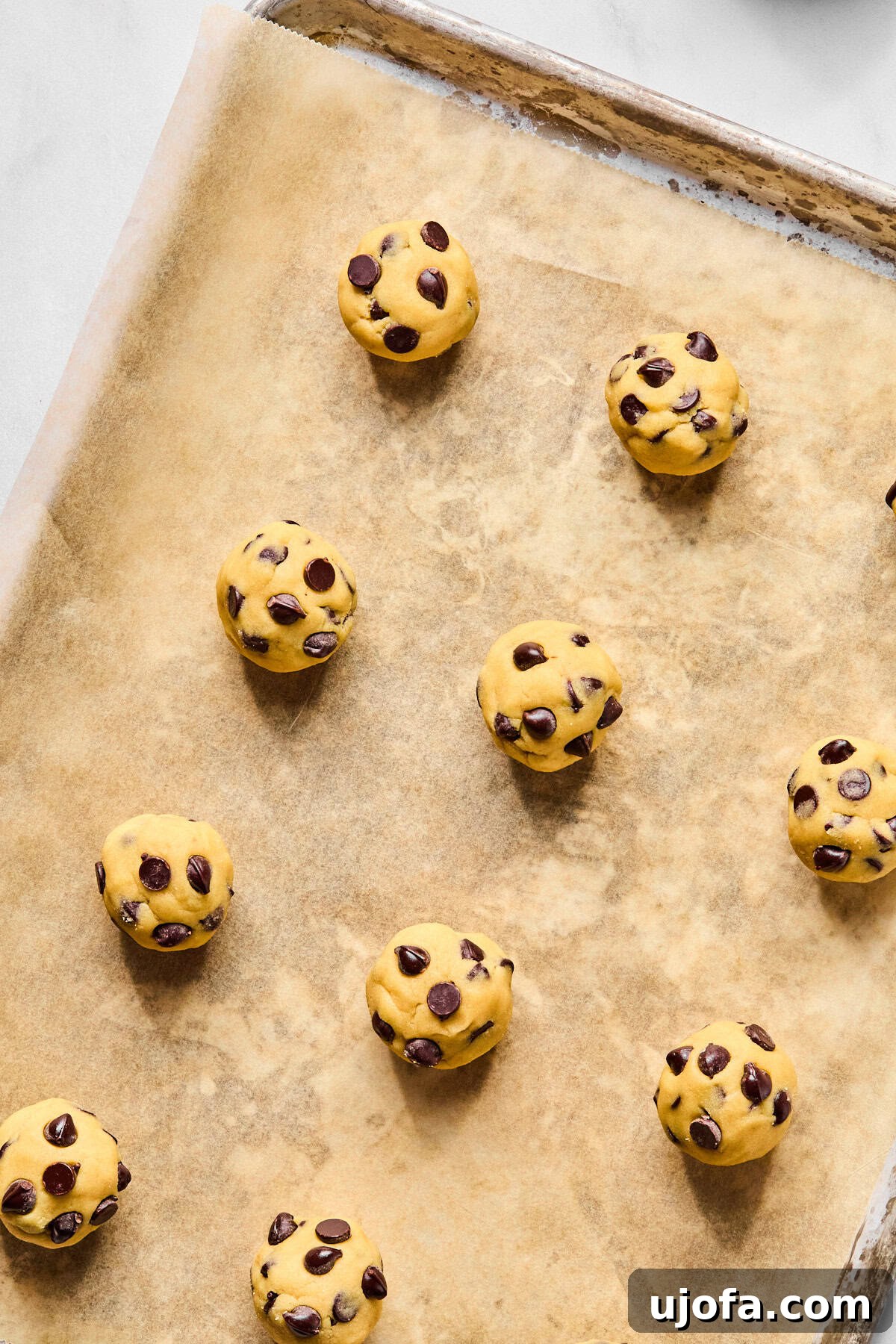 Raw cookie dough balls perfectly scooped and placed on a parchment-lined baking sheet, spaced apart.