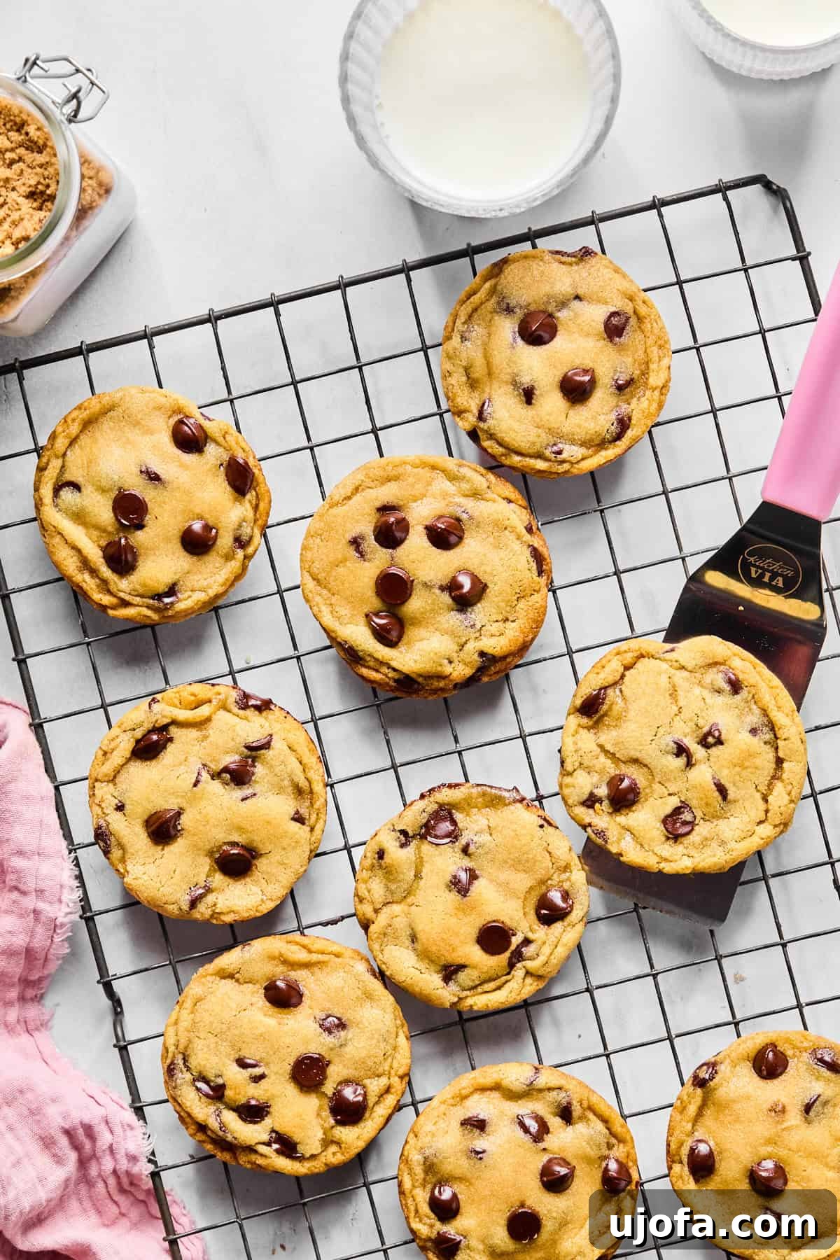 Freshly baked cookies cooling on a wire rack, with a pink spatula beside them.