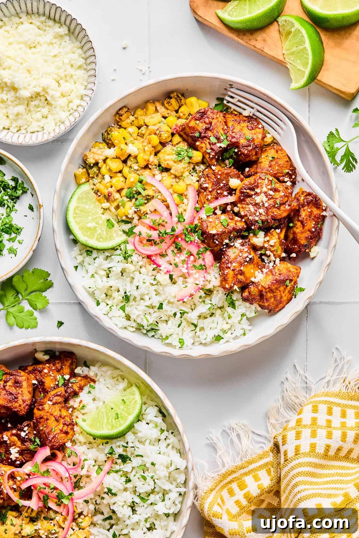 Two vibrant street corn chicken rice bowls beautifully garnished with fresh cilantro and a lime wedge, with a fork resting inside the main bowl, ready to be enjoyed.