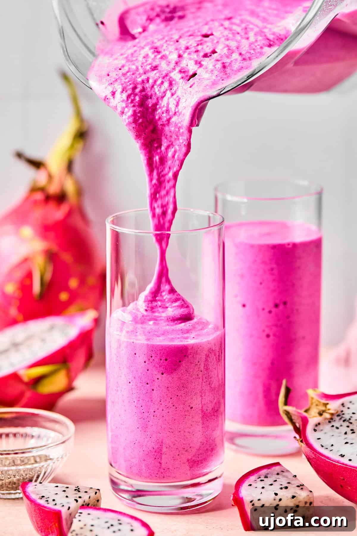 Dragonfruit Power-Up Smoothie 6 Dragonfruit smoothie being poured into a tall glass with another full glass behind it and sliced dragonfruit scattered around.