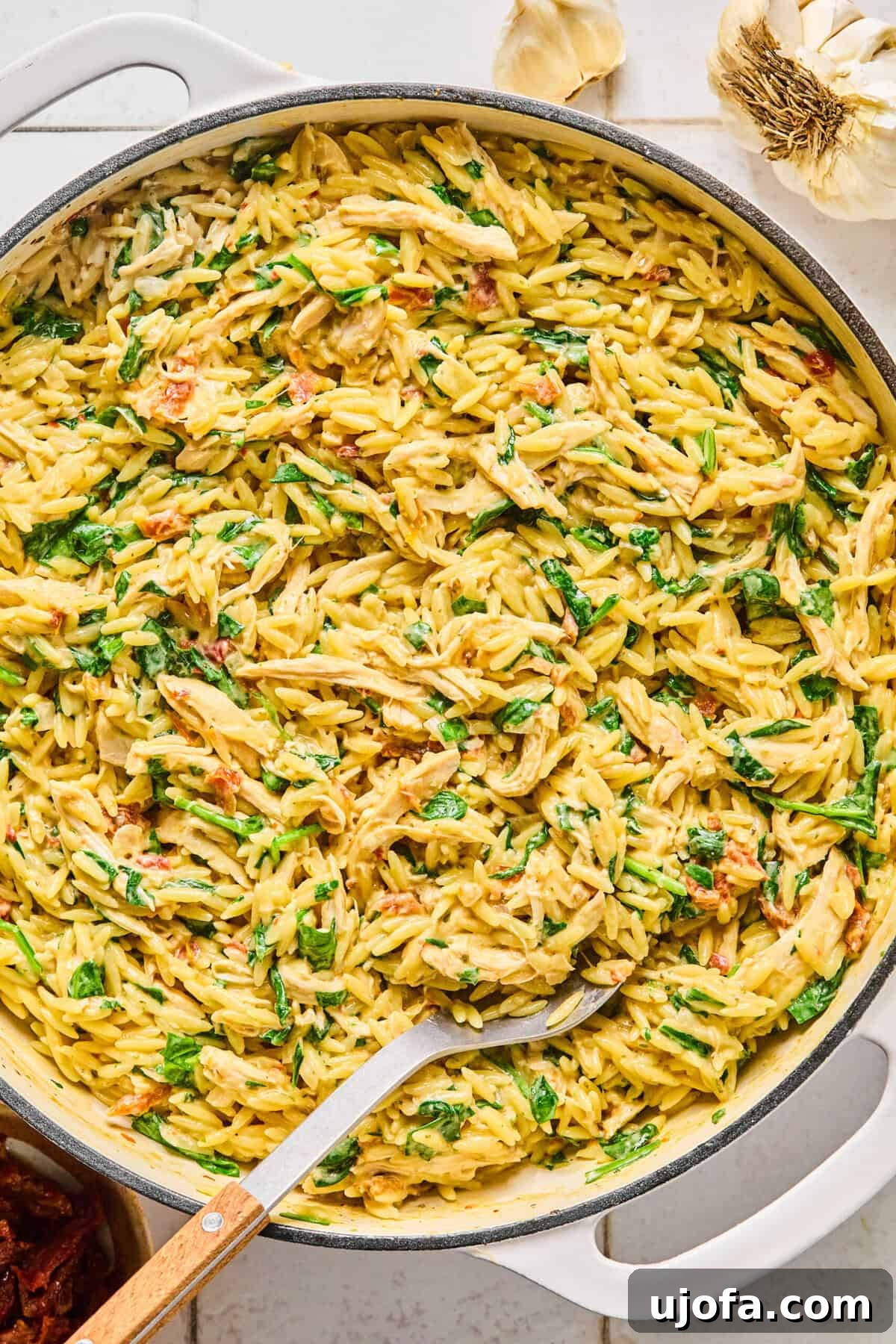 Marry Me Chicken Orzo garnished with fresh basil and grated parmesan with a serving spoon resting in it.