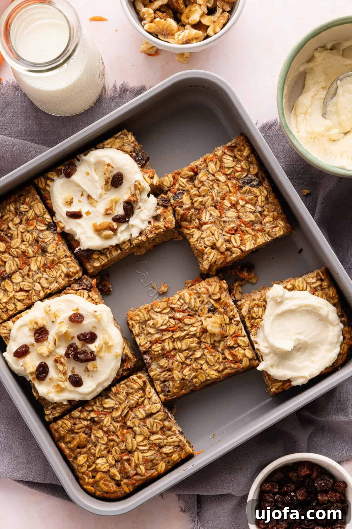Protein-Packed Carrot Cake Oatmeal Bake 9 Sliced carrot cake baked oats; 3 of the slices have protein cream cheese frosting on them and are topped with raisins and walnuts.